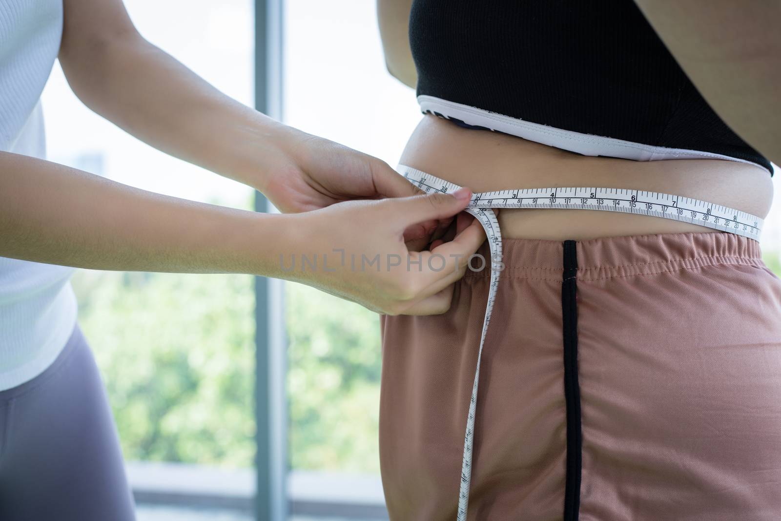 Young female trainer measuring fat layer of overweight woman with waistline at fitness