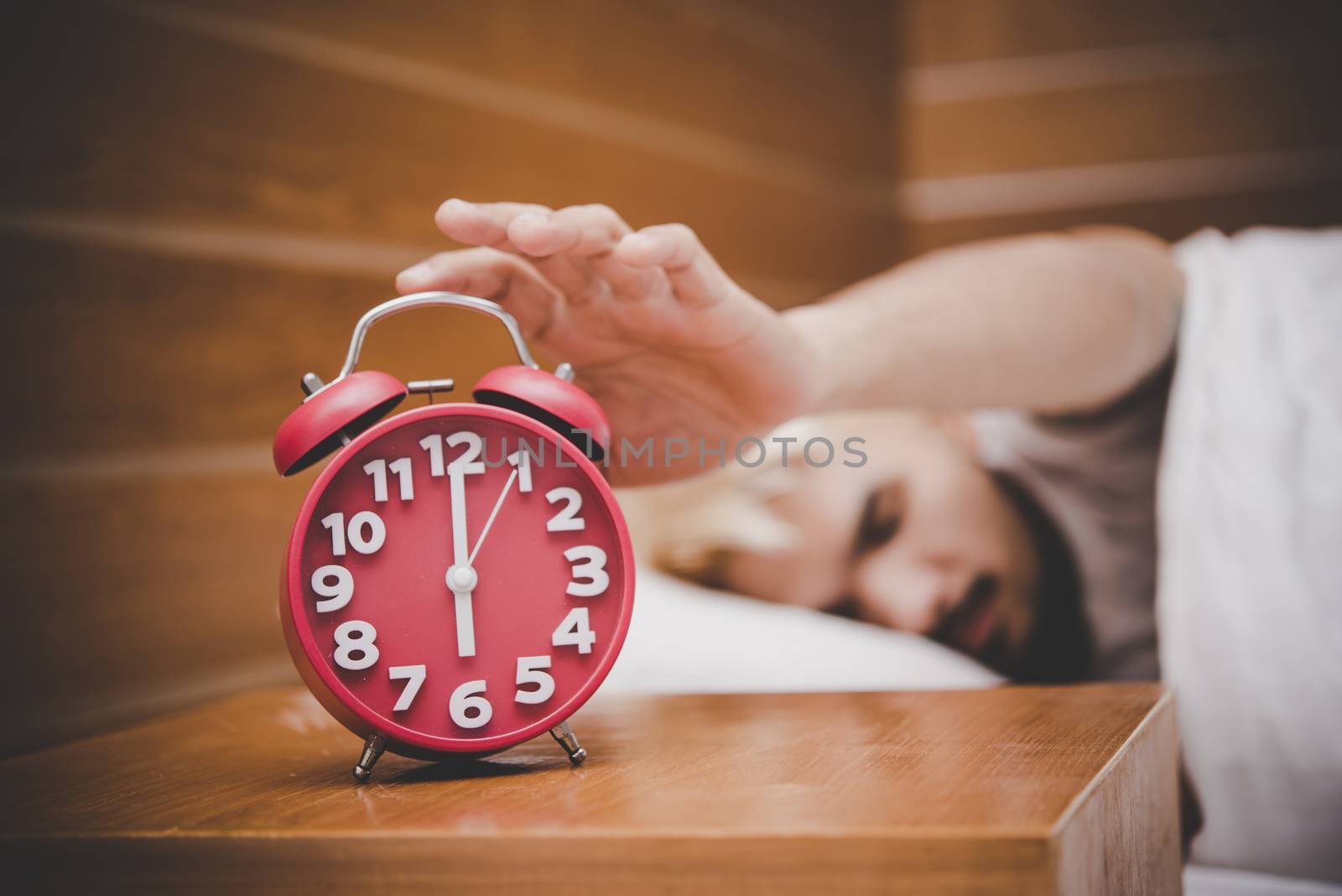 Man trying to turn off the alarm clock waking up at morning.