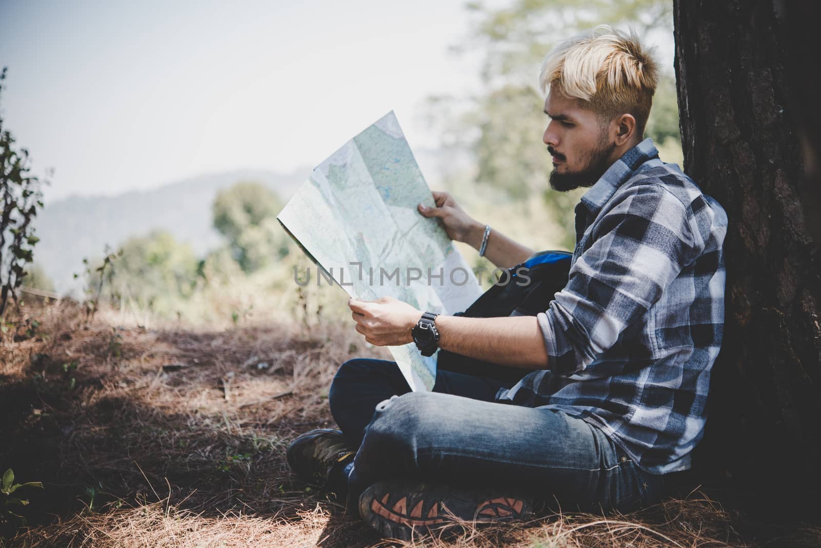 Hiker relaxing by tree looking at map, go adventure in mountain.