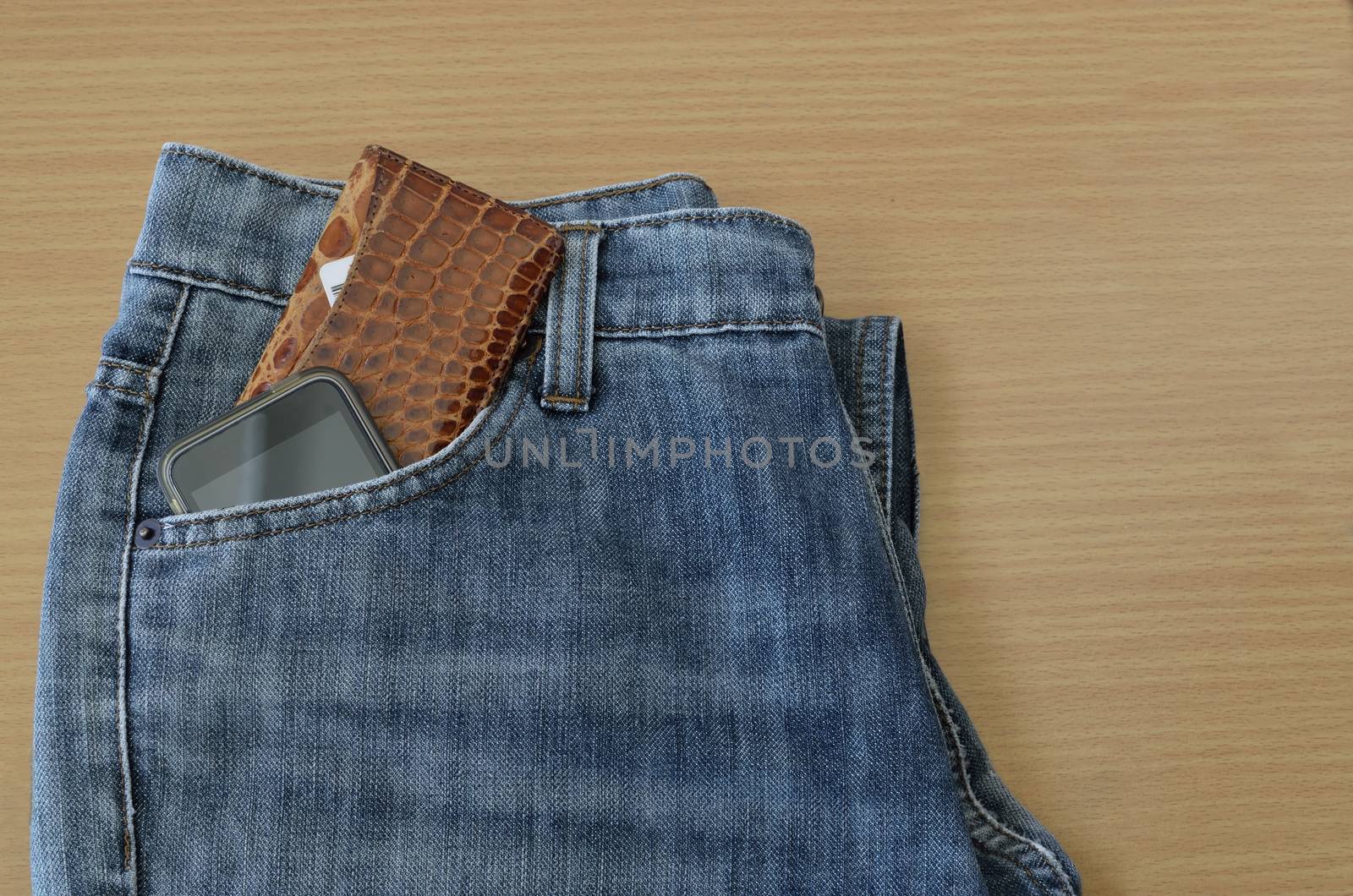 leather wallet and smart phone in jeans pocket on wooden background