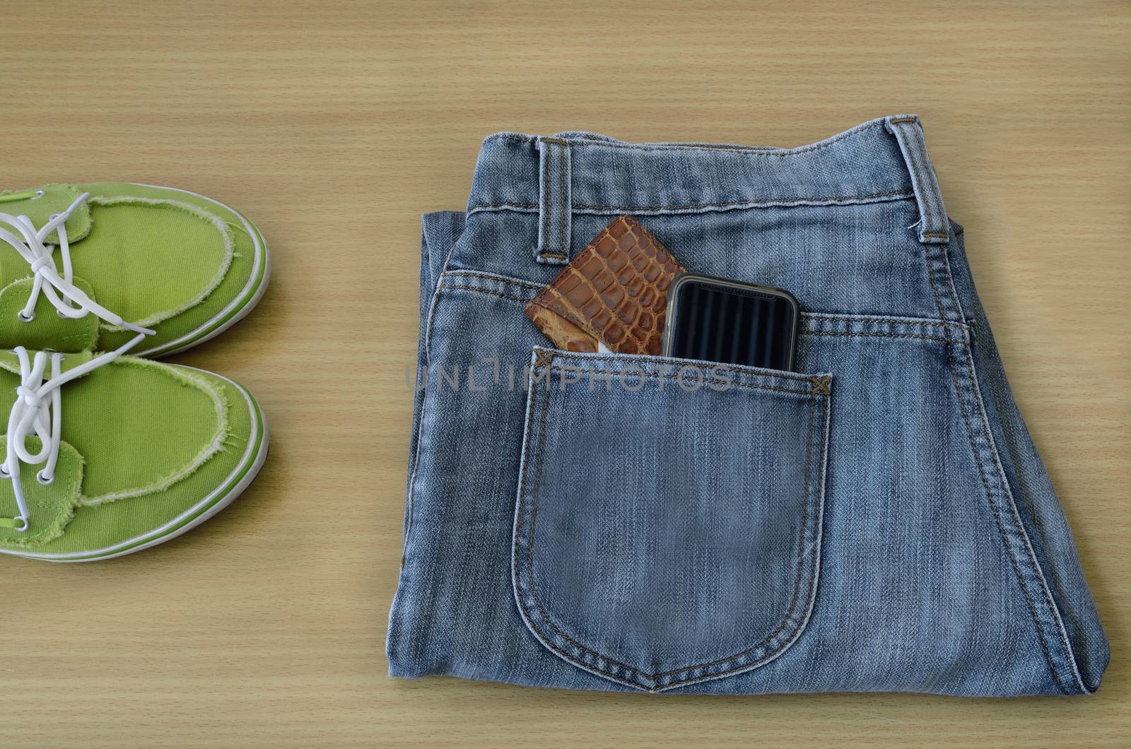 leather wallet and smart phone in jeans pocket,  sneakers on wooden background