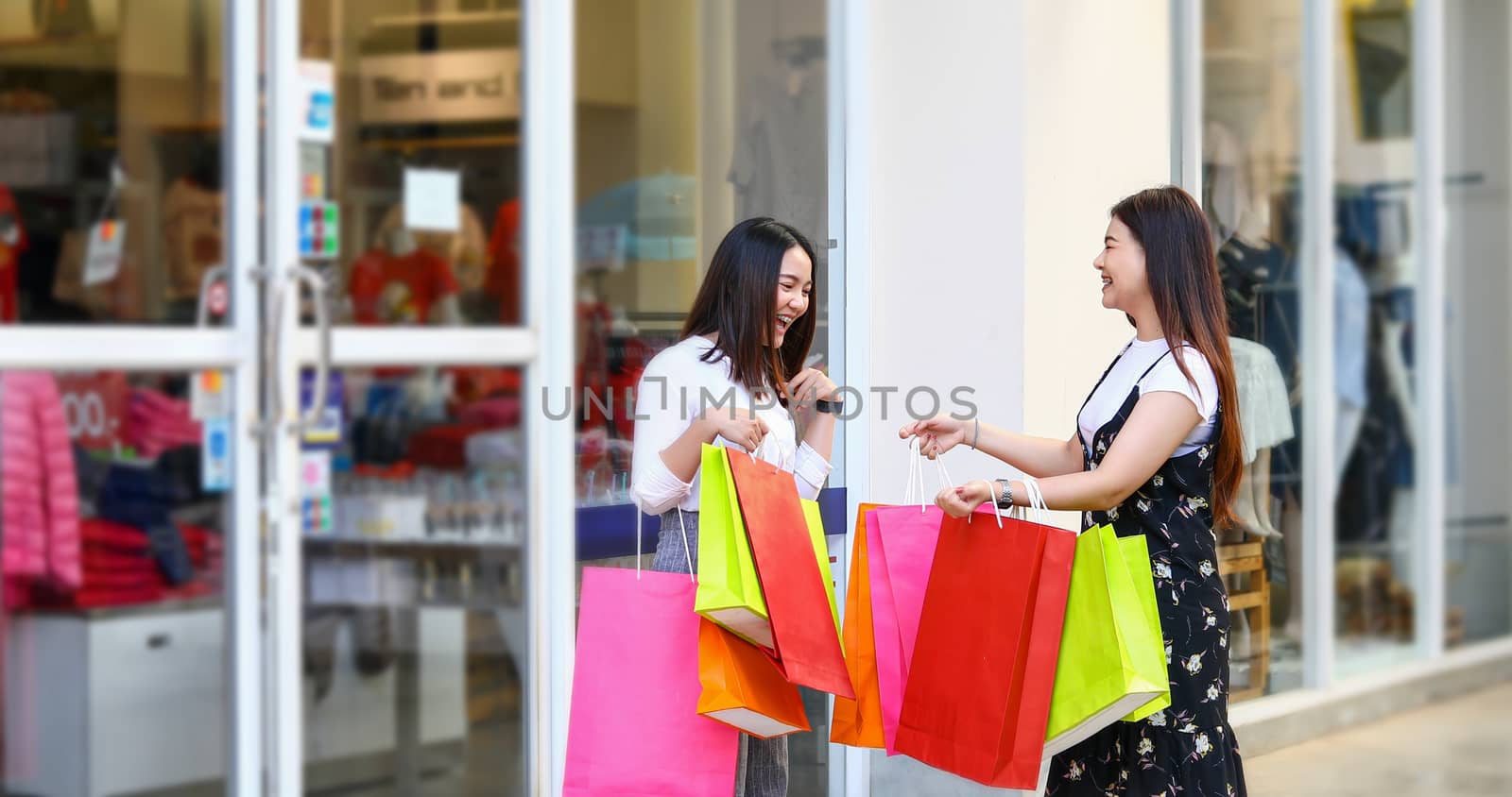 Asian women with friend are holding shopping bags and using a smart phone and smiling while doing shopping in the supermarket/mall by Tuiphotoengineer