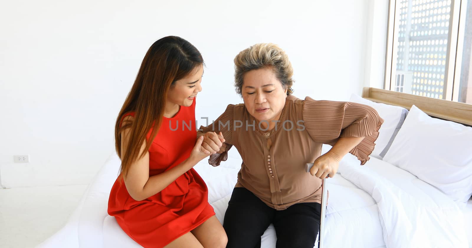 Cheerful woman taking care of her grandmother in bed room at home