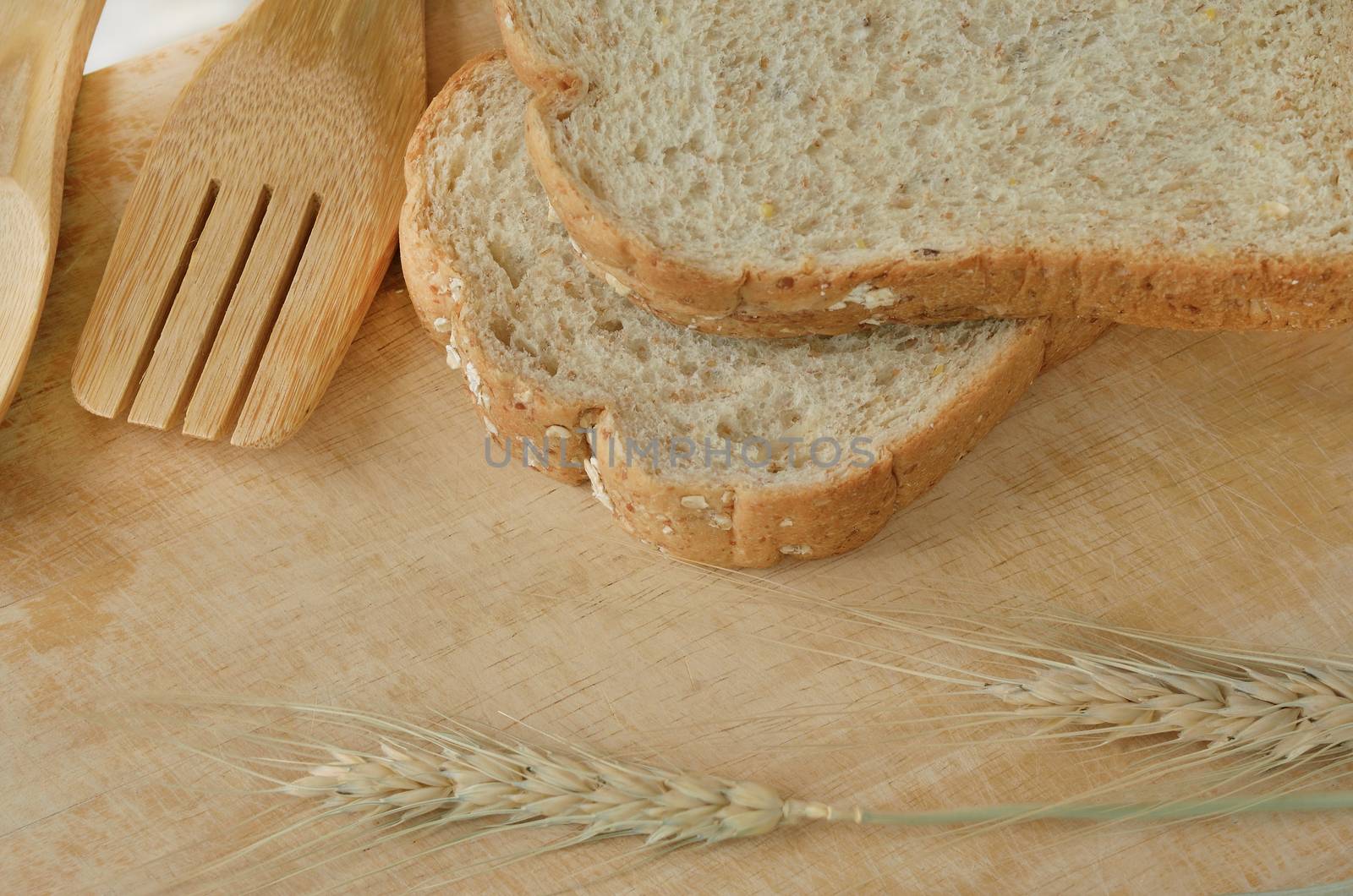 Wooden kitchen utensils with bread and barley on wooden background
