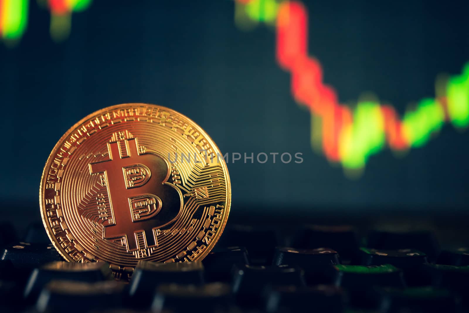 A golden coin with bitcoin symbol on computer keyboard with stock graph background.