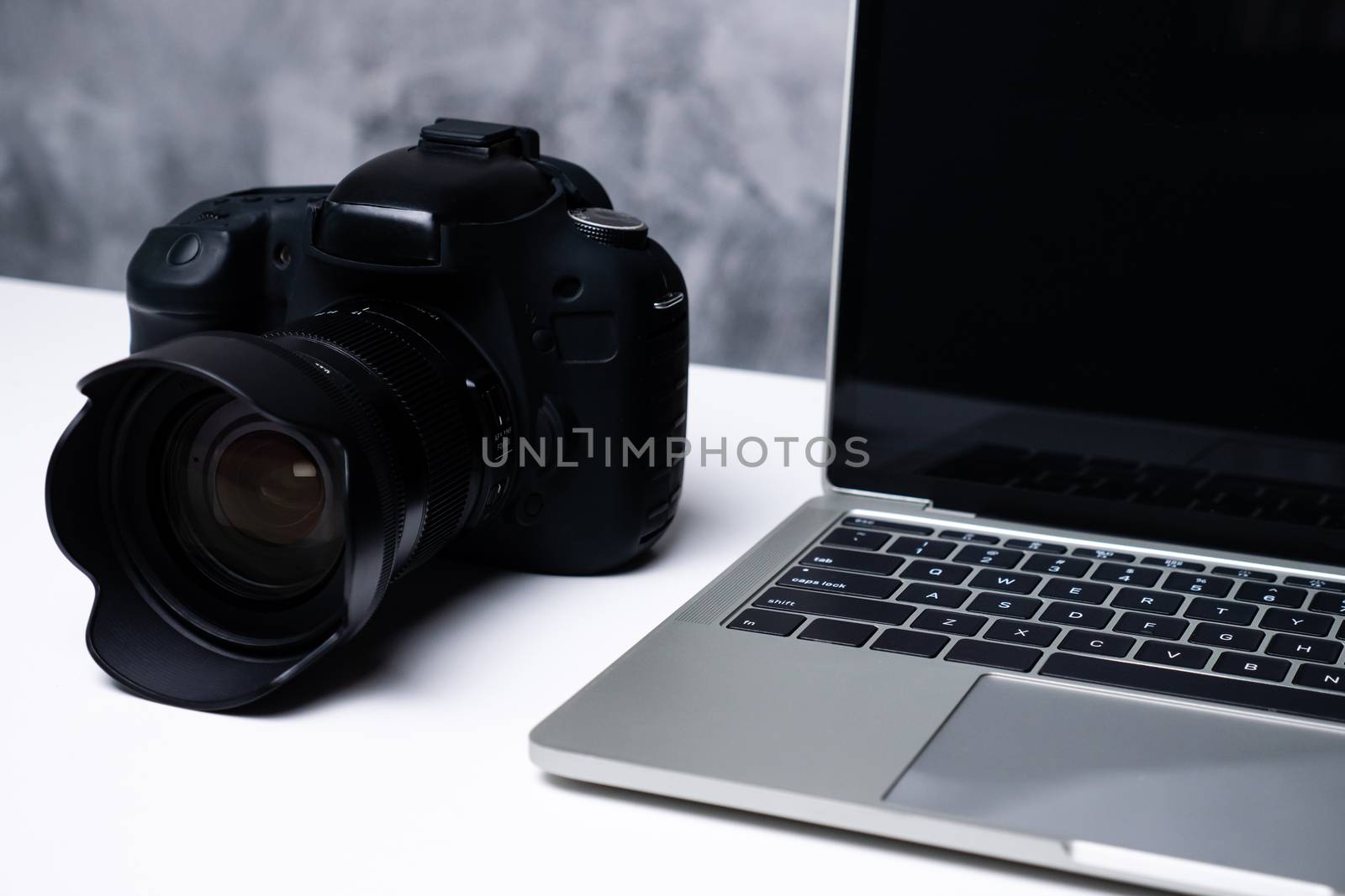 A black digital camera and a computer laptop on a table.