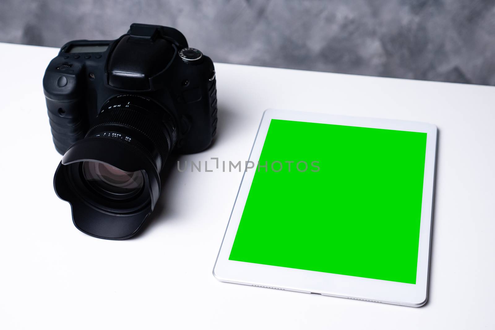 A black digital camera and a blank screen tablet on a table.