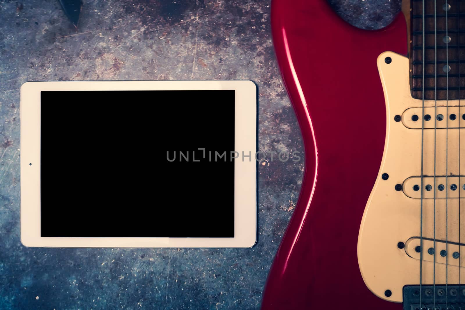 Tablet and electric guitar on a grunge background.