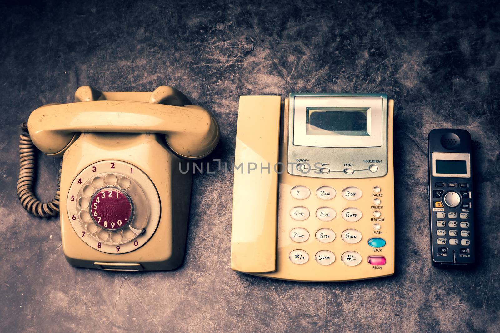 An old telephone with rotary dial, a landline and obsoleted cellphone on a grunge background.