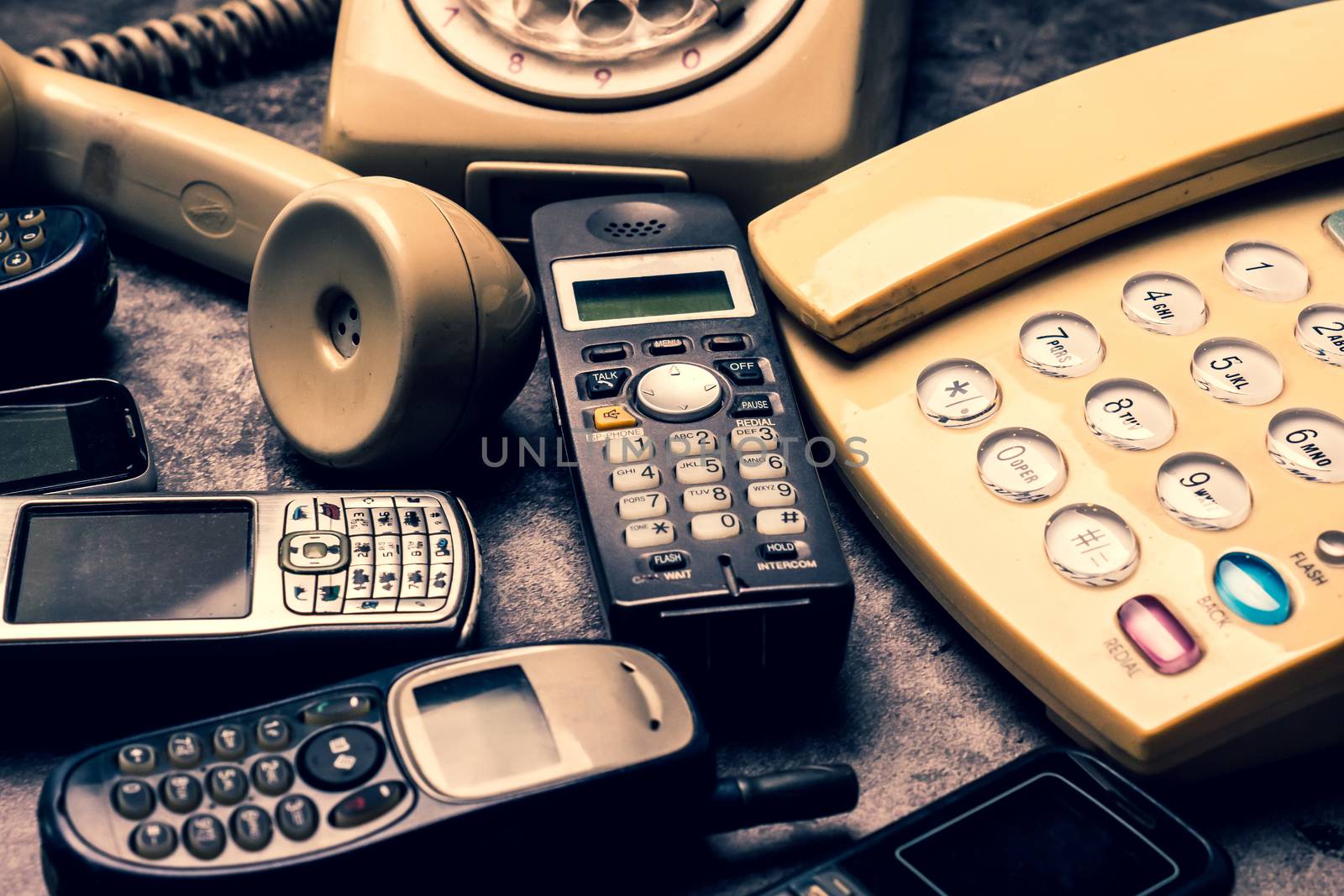 An old telephone with rotary dial, landline and obsoleted cellphone on a grunge background.