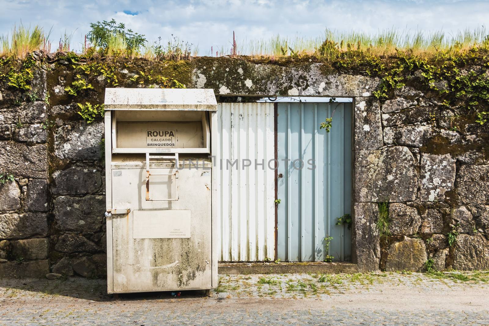 Vila Cha near Esposende, Portugal - May 9, 2018: Public containers for retrieving toy and clothes (Roupa Brinquedos) in front of a stone wall in the city center on a spring day