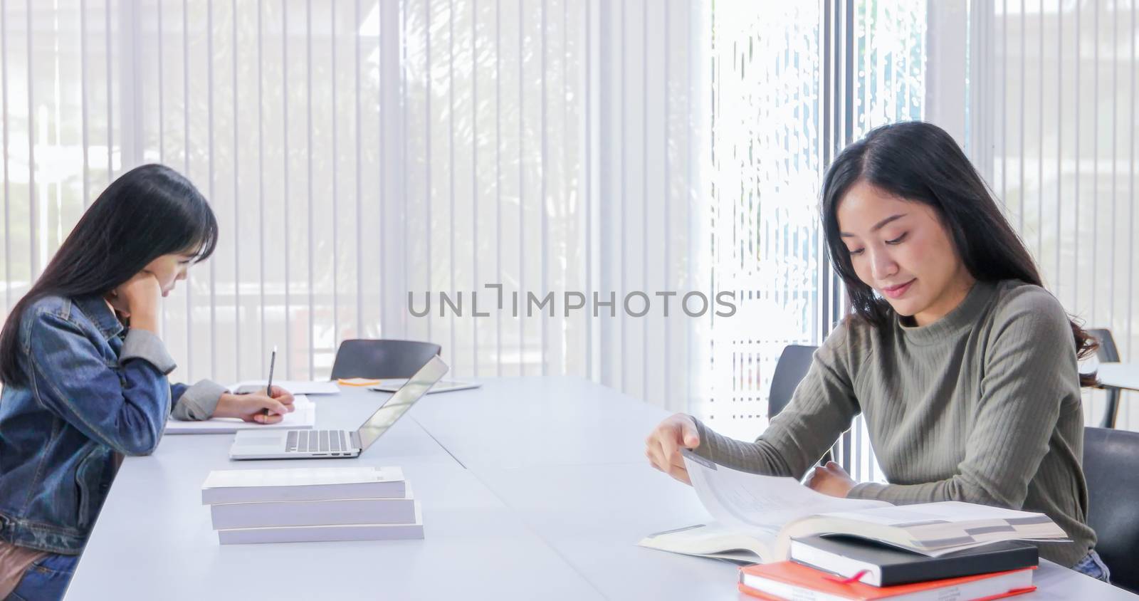 Asian women Students Smile and reading book and using notebook for helps to share ideas in the work and project. And also review the book before the exam