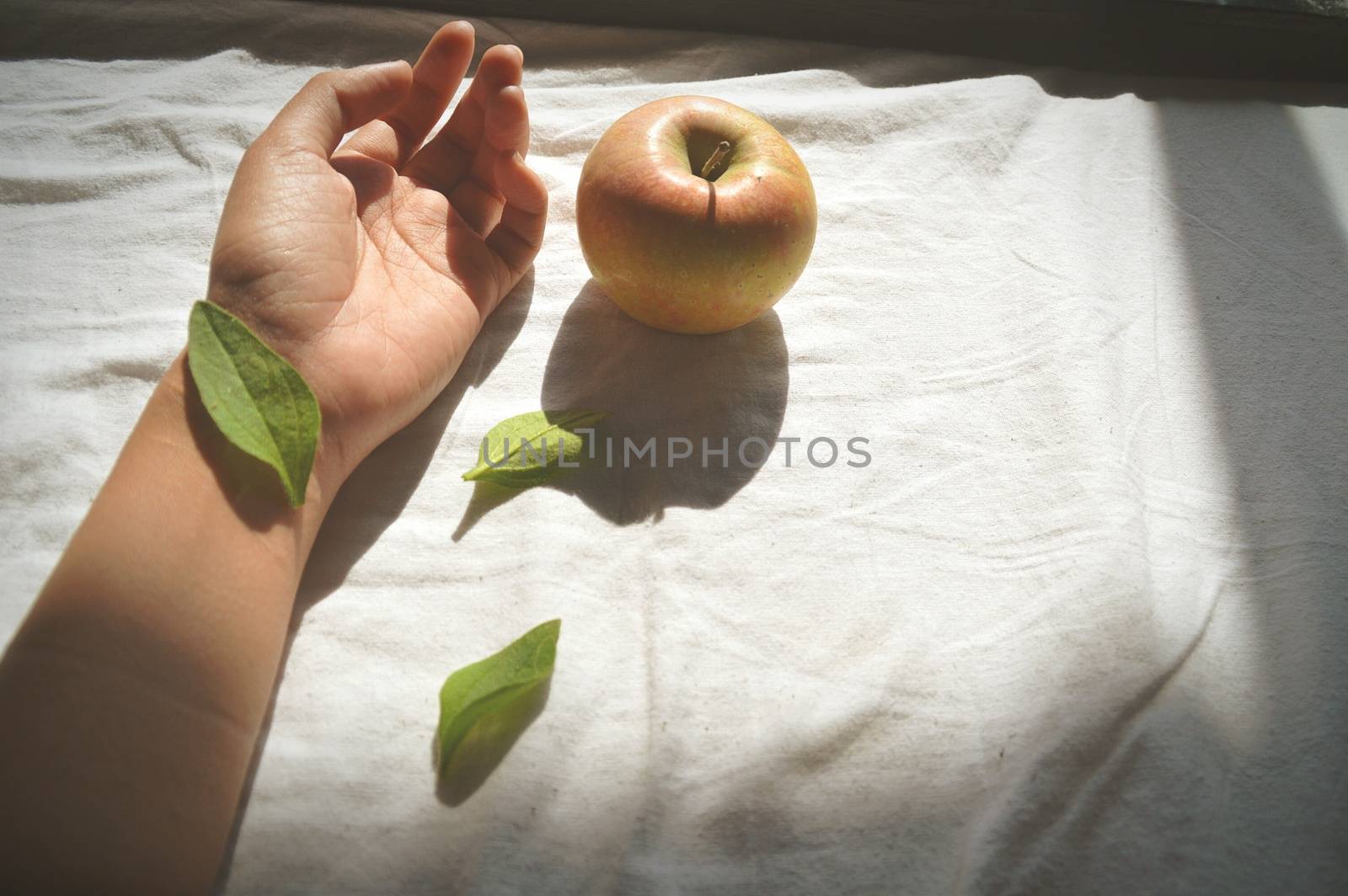 Leaf covering the wrist hand and an apple against a white bed sheet showing concept of Mental Health and Suicide Prevention
