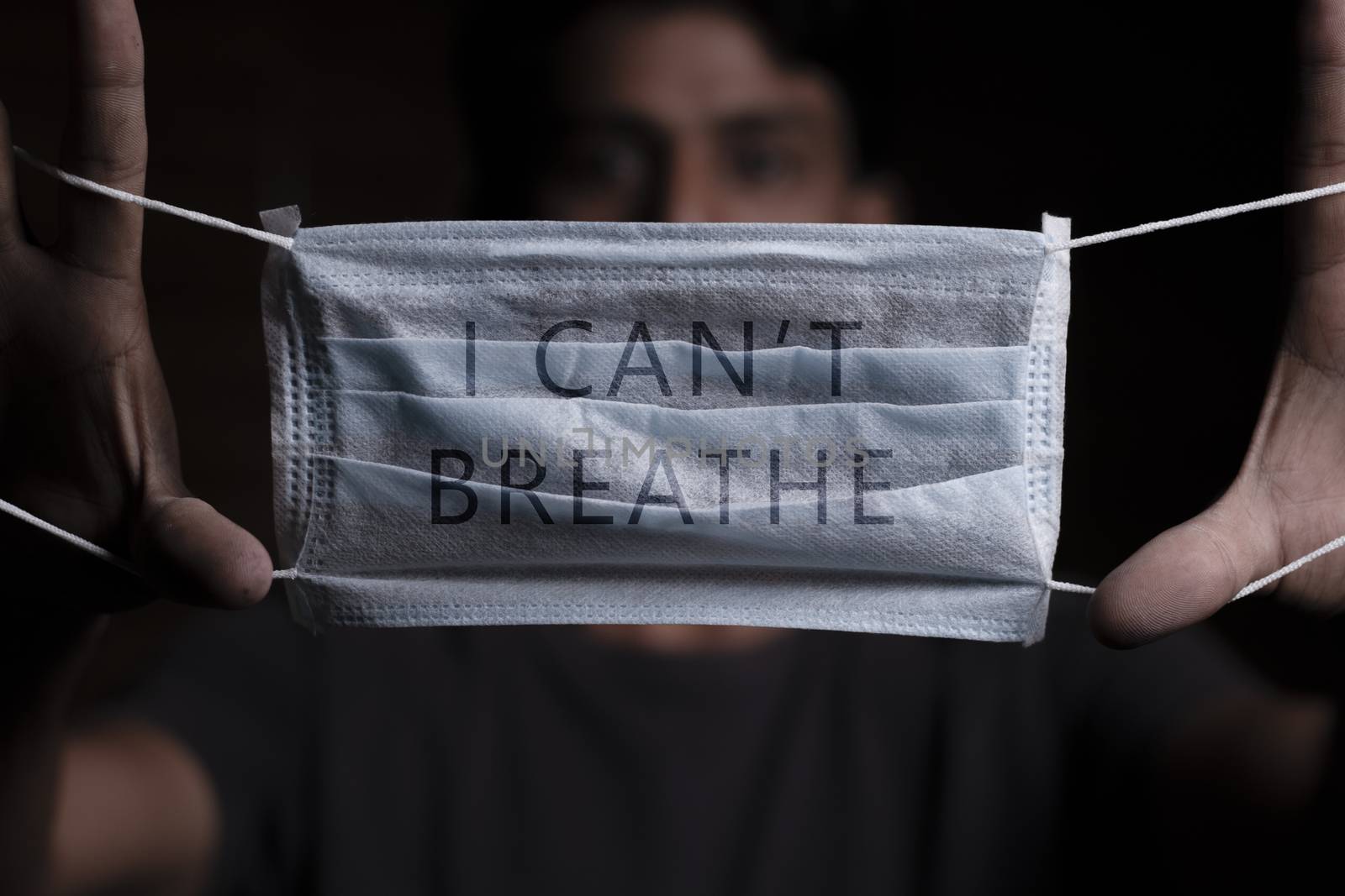 Young man holding medical mask with I Can't Breathe inscription on it. Cooncept of Protest about racial discrimination of Black People in U.S. America. by lakshmiprasad.maski@gmai.com