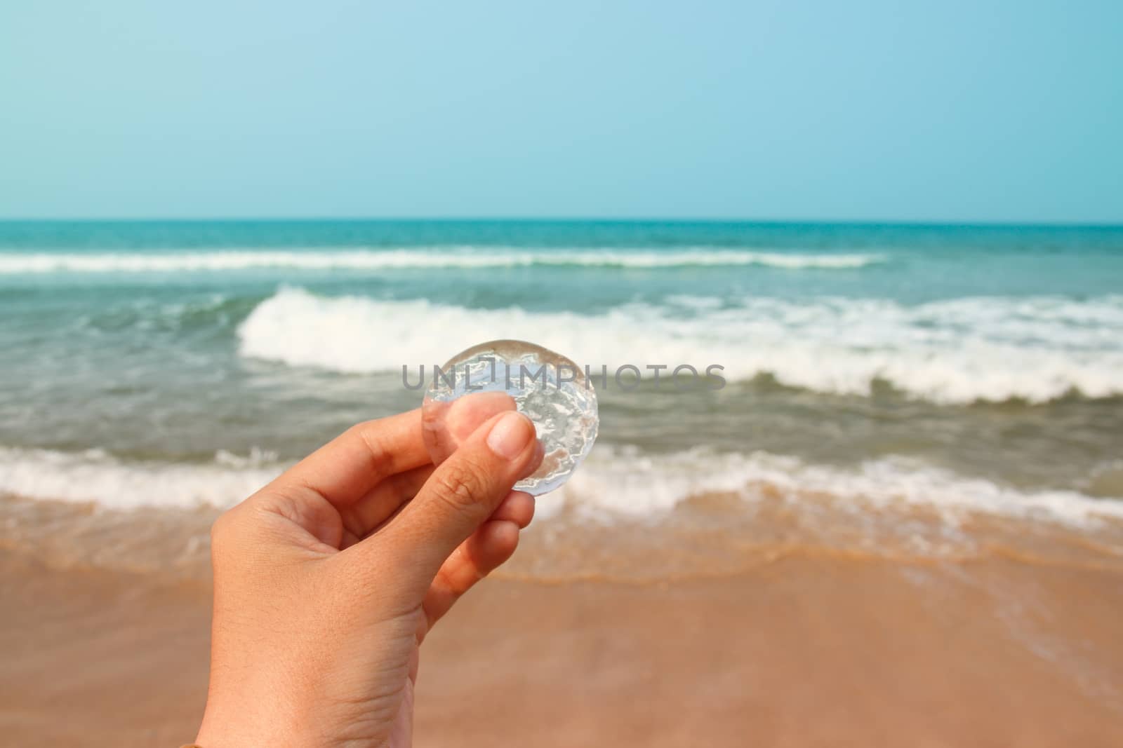 Hand holding a glass against the blue sea showing Summer at the beach