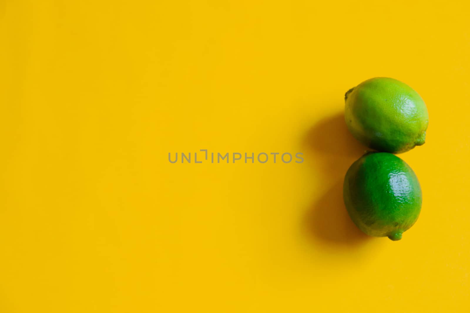 Two green limes against yellow background showing concept of happiness, summer, positivity and life