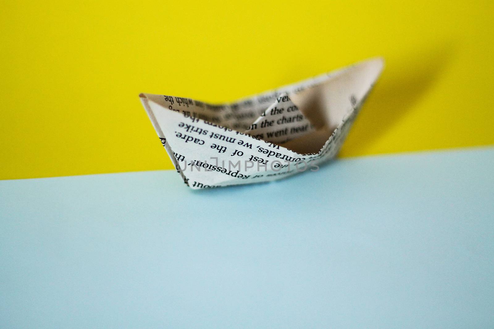 A paper boat made from old newspaper page against blue colored paper showing the concept of childhood dream, aspirations, hope and finances