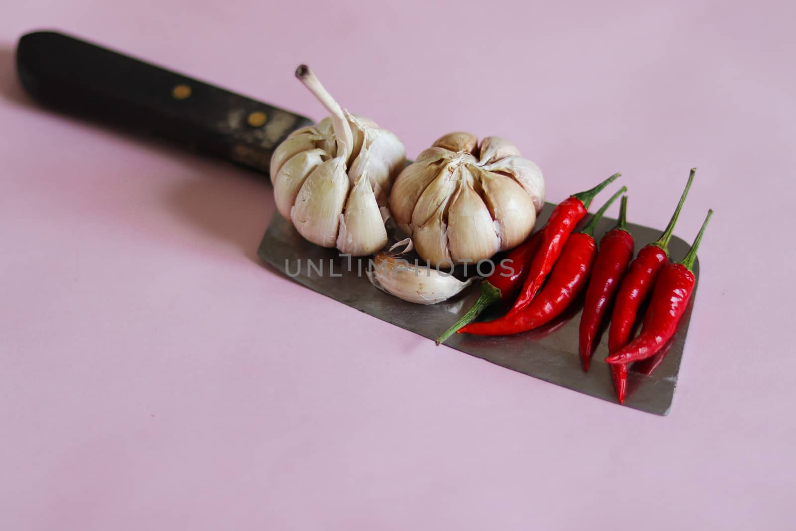 Garlic bulbs and red chilies on a knife against a pink background to show concept of gastronomy, cuisine, cooking and food industry