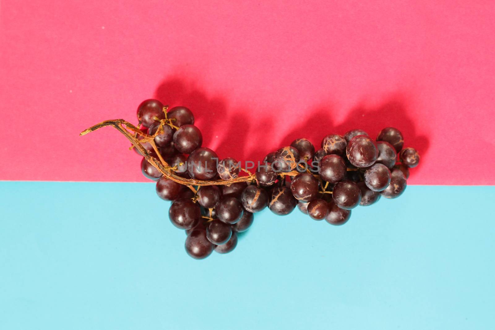 Red grapes against vibrantly colored pink and blue background to depic summer