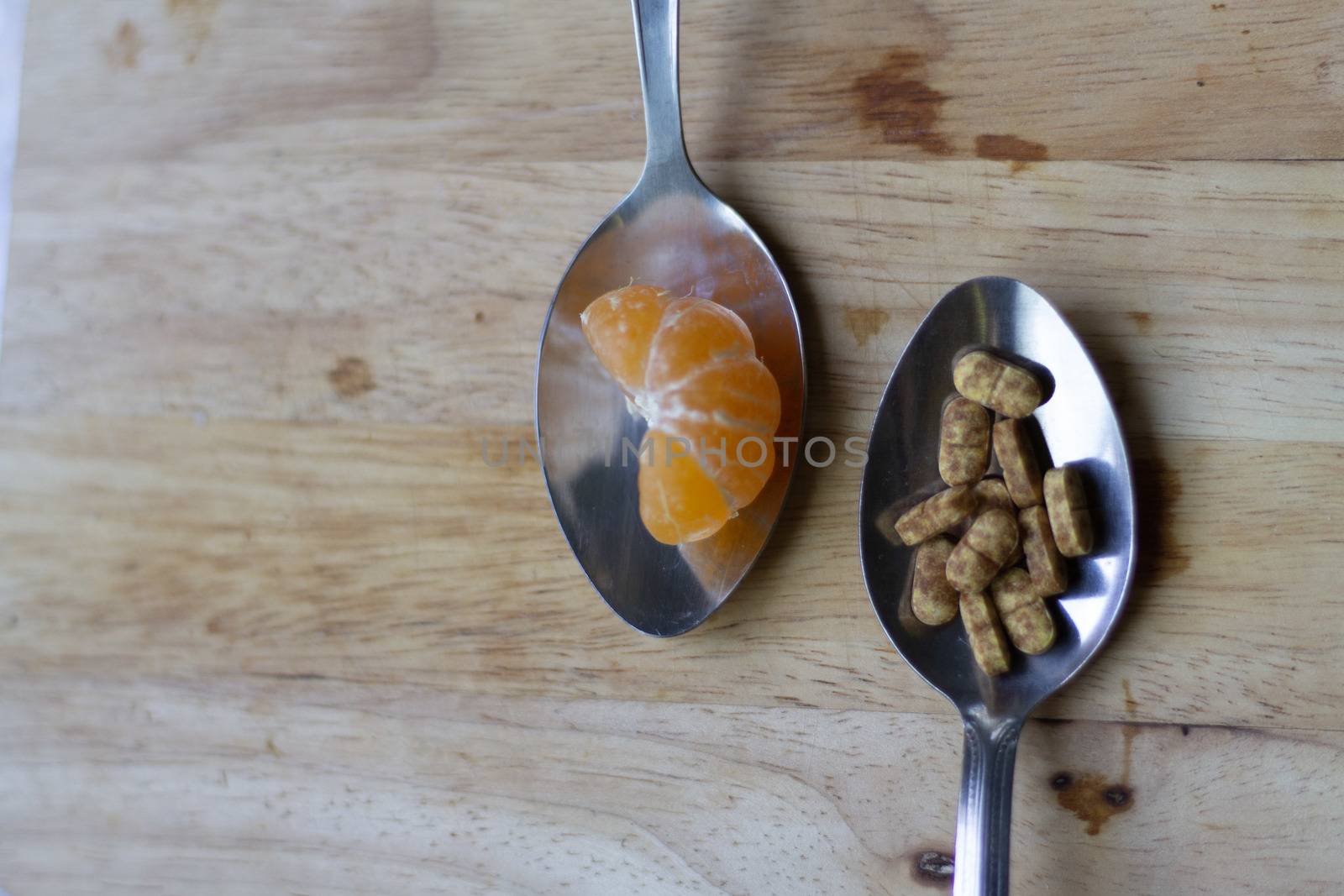 Top view of spoonfuls of orange and Vitamin c tablet to show the comparison between natural and artificial ascorbic acid source