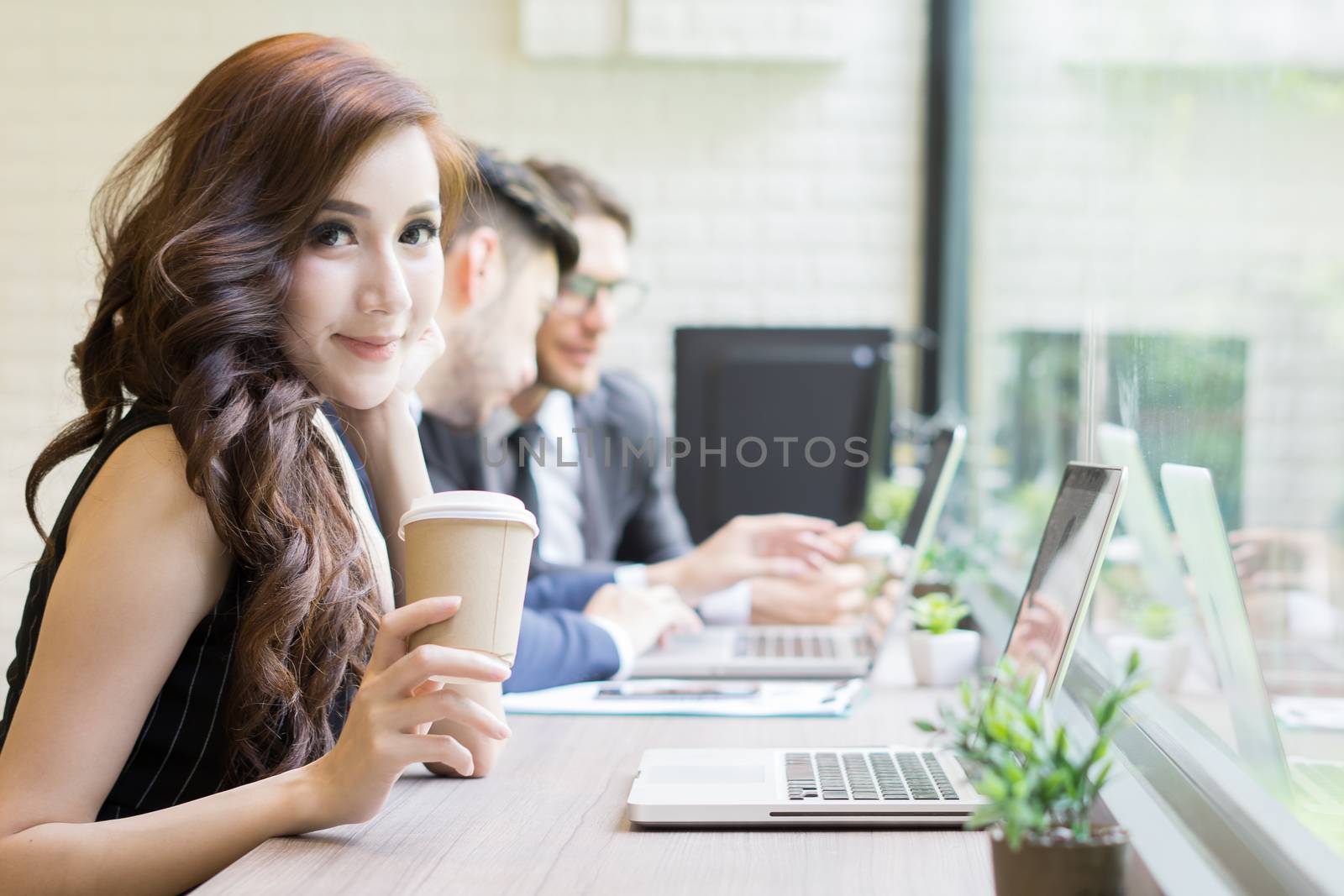 Businesswoman drinking coffee break  while coworker interacting in the background in the office
