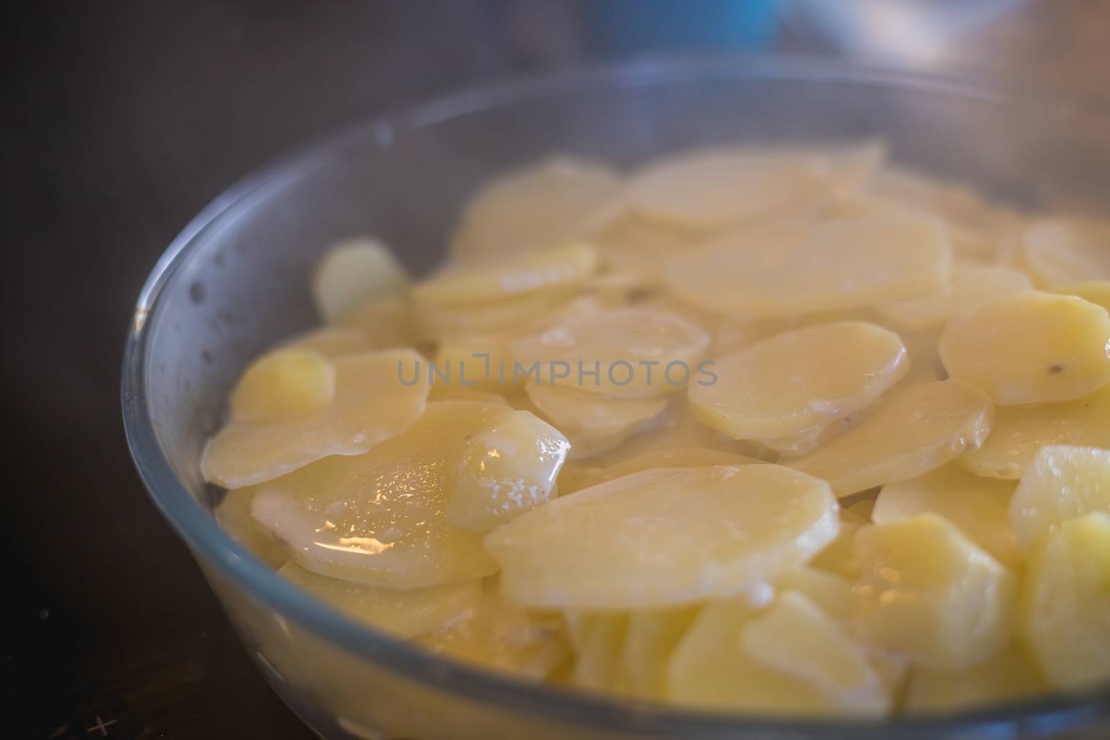 preparation of a gratin dauphinois with its potatoes, its cream and its condiments in a pan on the worktop of a kitchen