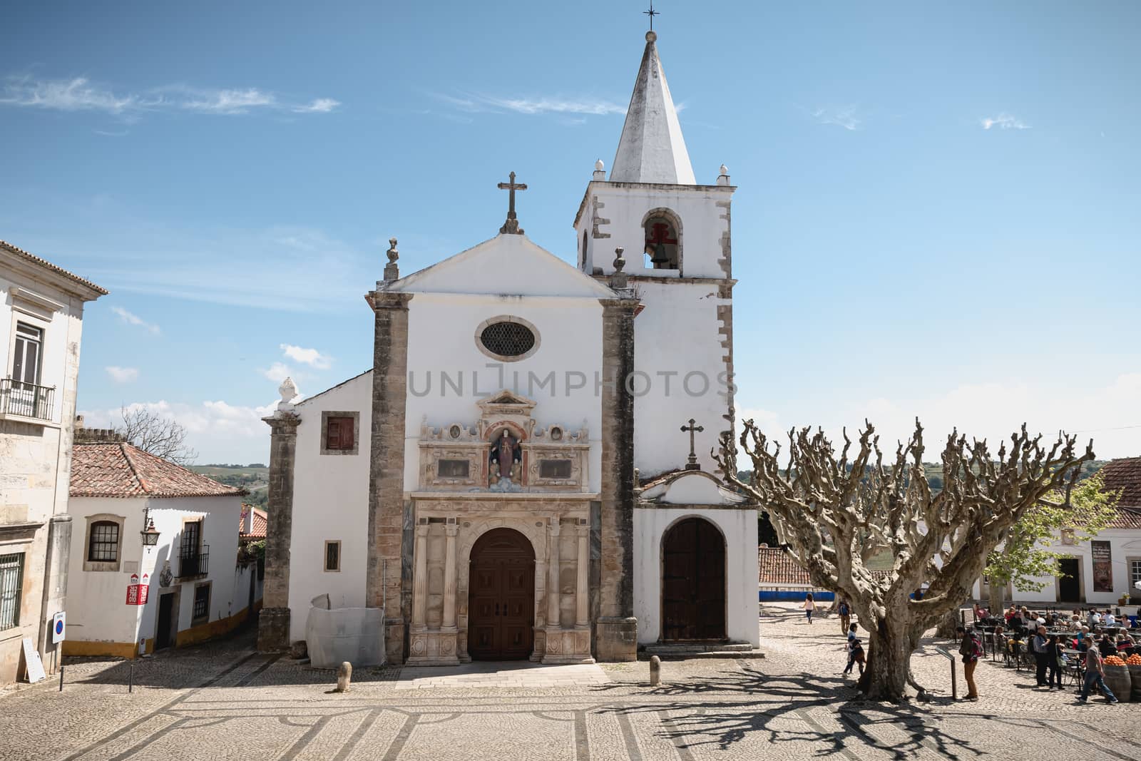 Obidos, Portugal - April 12, 2019: people walking around the Church of Saint Mary (Santa Maria) on a spring day