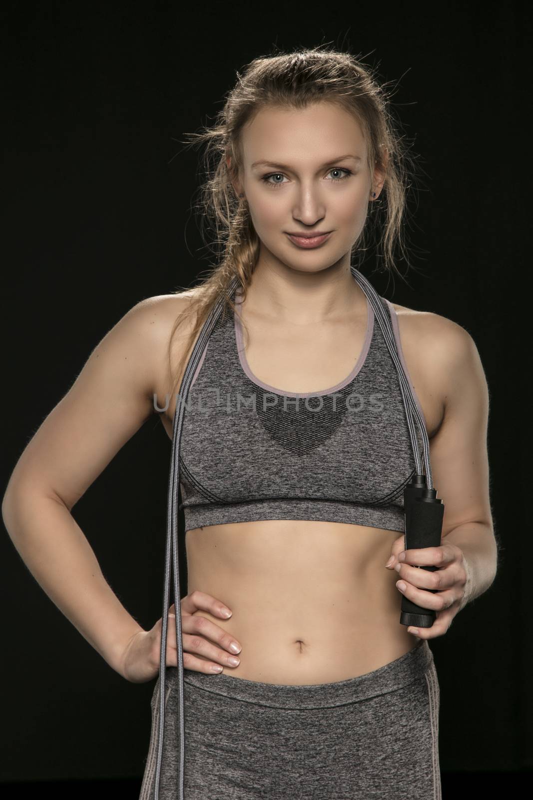beautiful athletic girl is practicing with a skipping rope, isolated on the black background