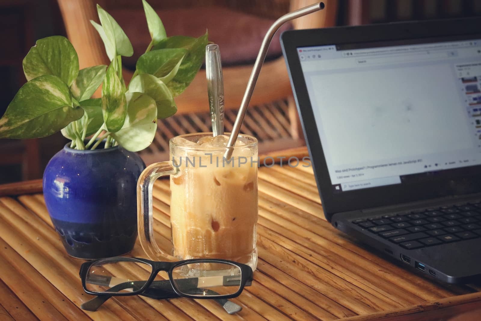 A laptop with iced coffee and reading glasses showing the concept of living the new normal by working from home to fight the spread of covid-19 pandemic