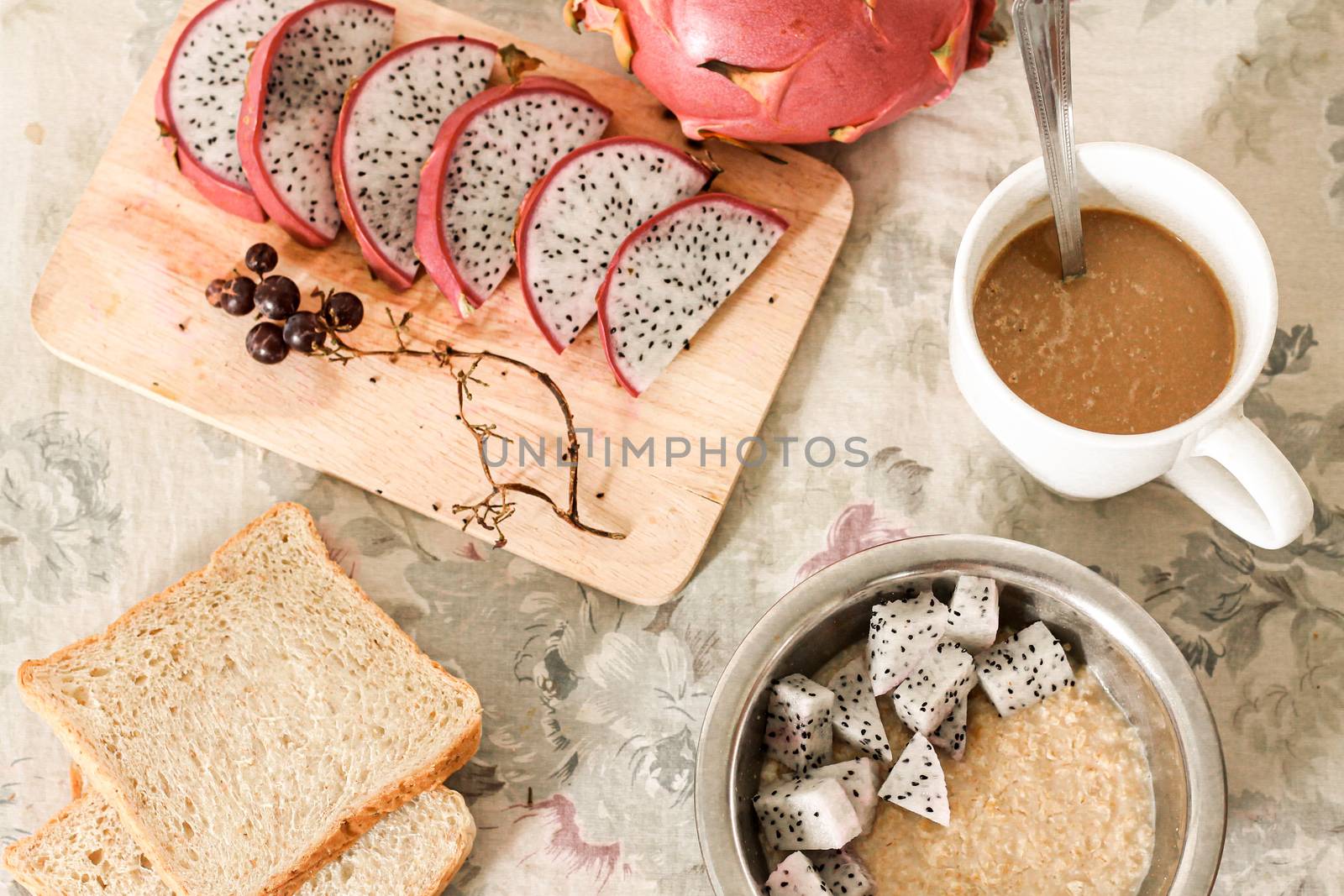 Healthy vegan breakfast of a bowl of oatmeal topped with dragon fruit slices served with whole wheat bread and coffee