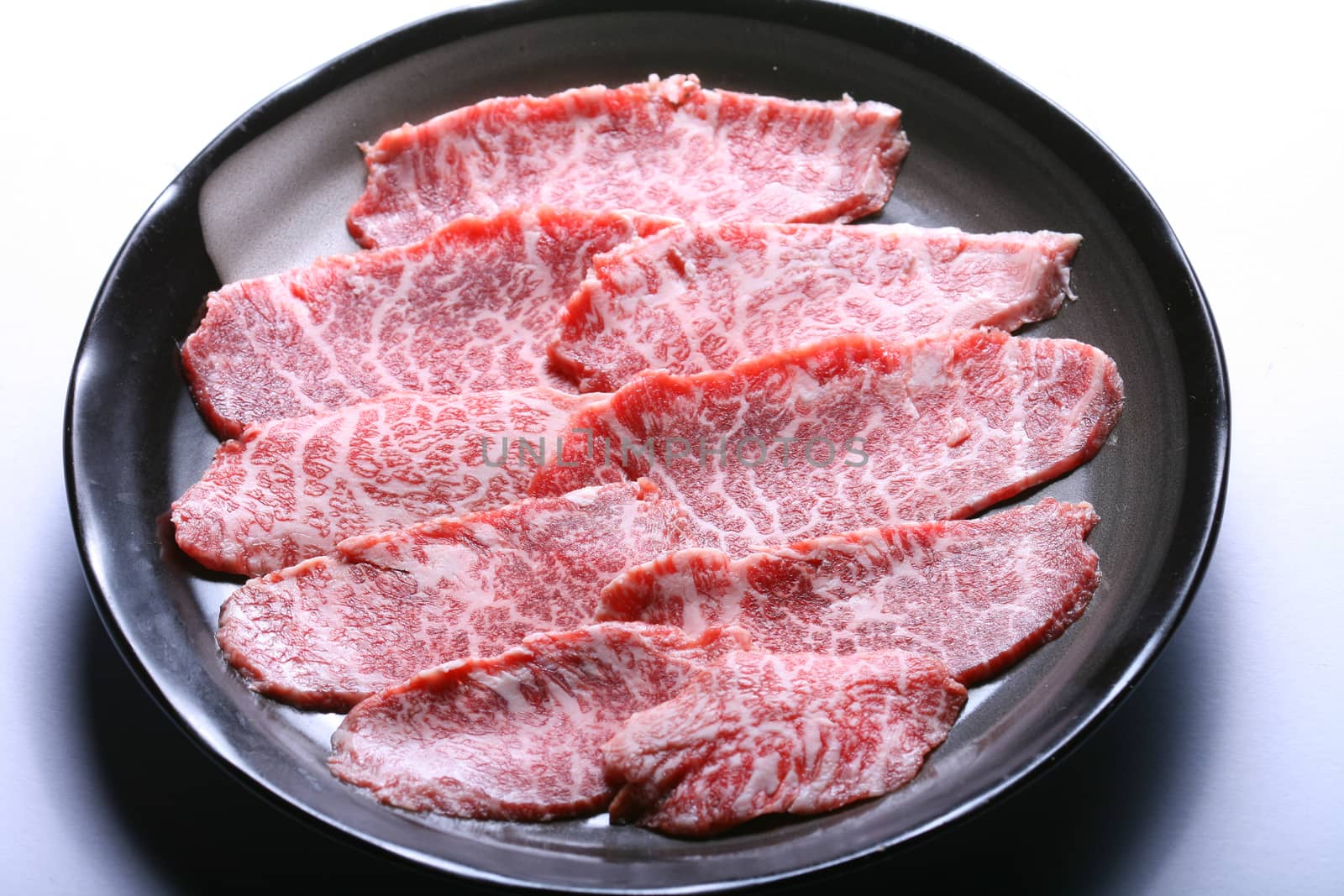 Raw Kobe wagyu beef sliced on black plate, white background