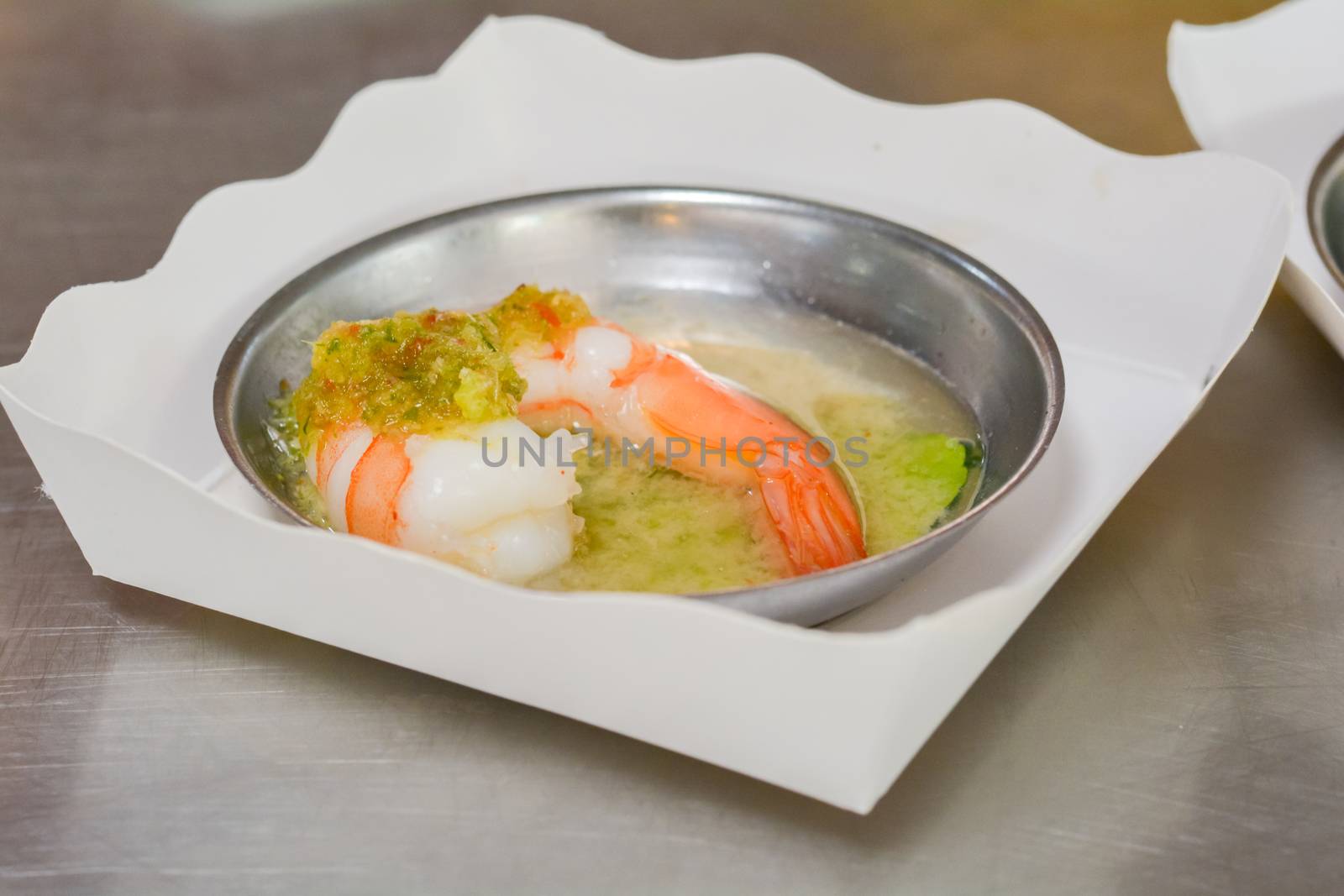 Steamed shrimp with seafood sauce and Thai herb in metal bowl on white paper plate in chinese restaurant.