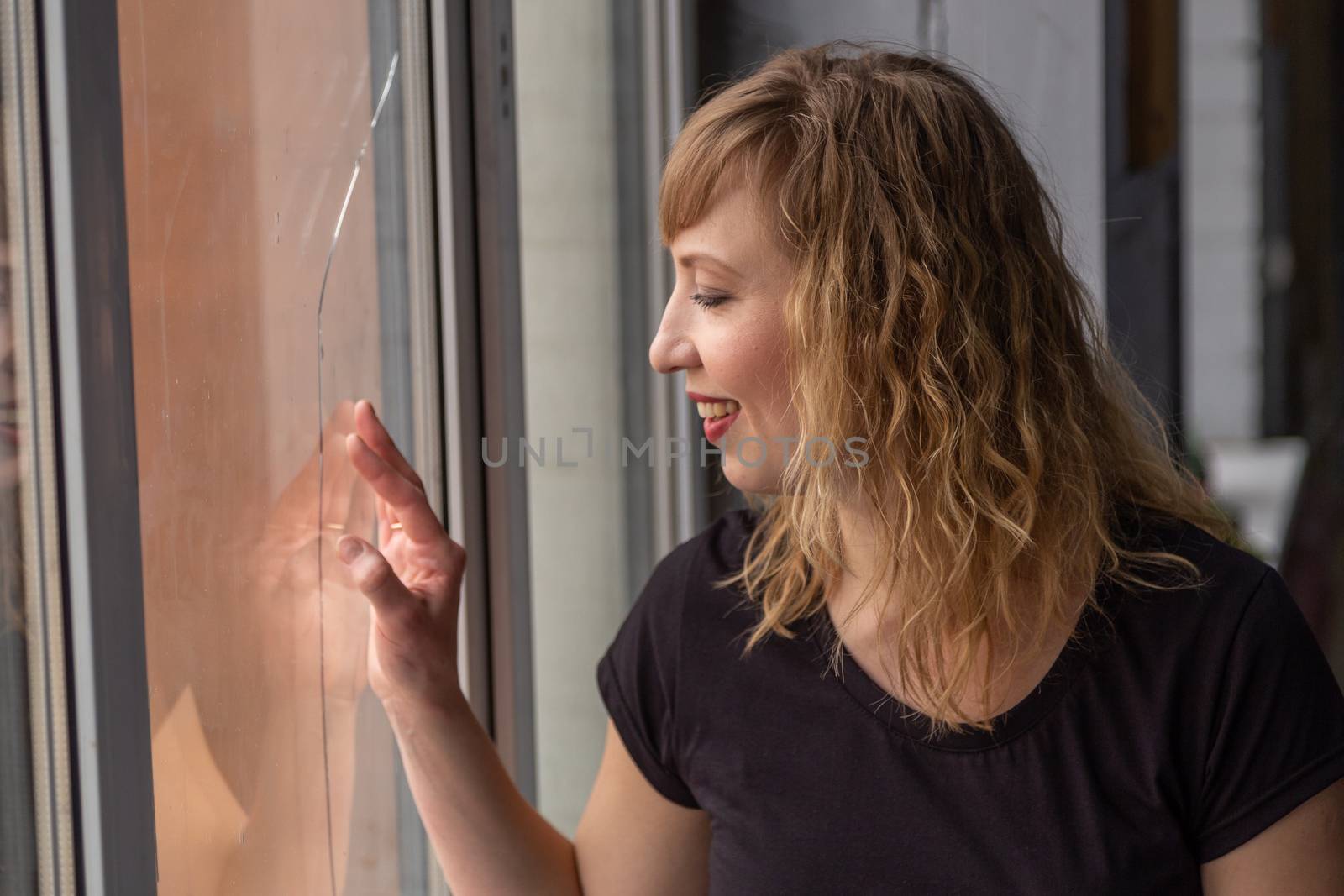 A woman of 30 years with blond hair near the window, you can see her reflection. Close-up