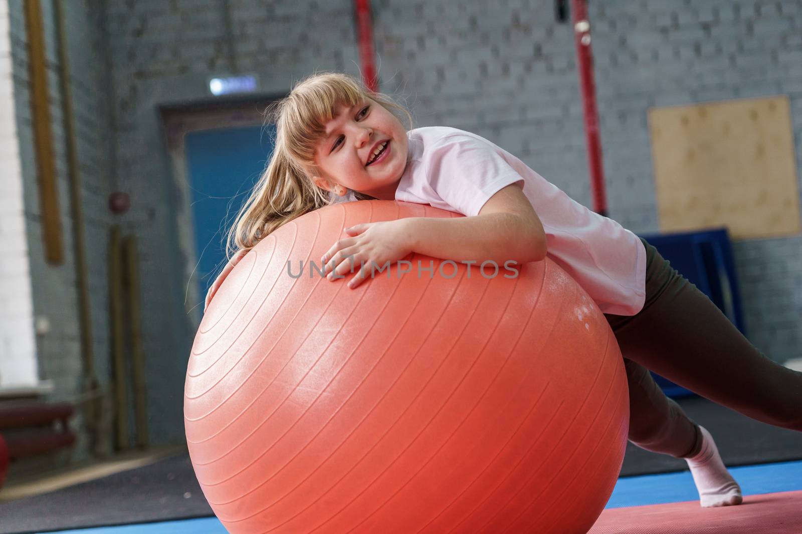 girl 8 years old with blond hair plays with a fitball in the gym
