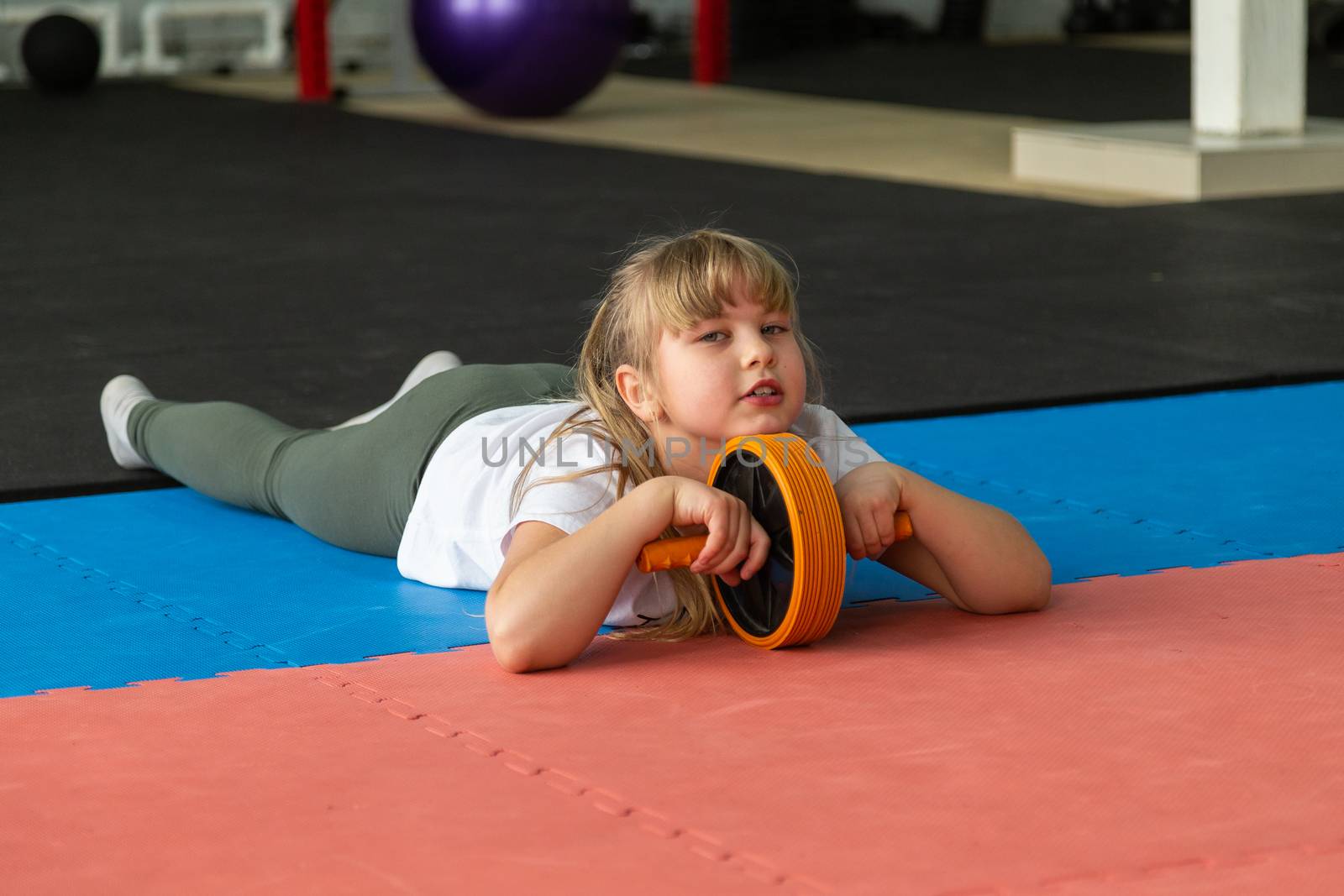 girl 8 years old with blond hair trains in the gym with a roller for the press