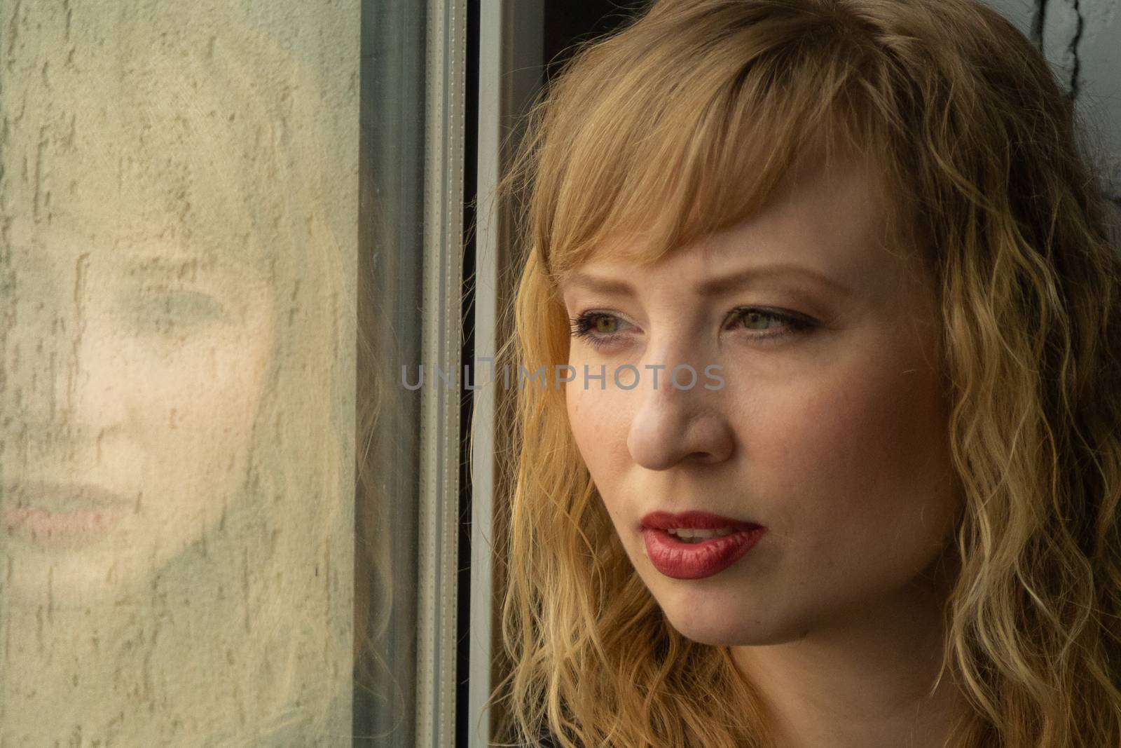 A woman of 30 years with blond hair near the window, you can see her reflection. Close-up