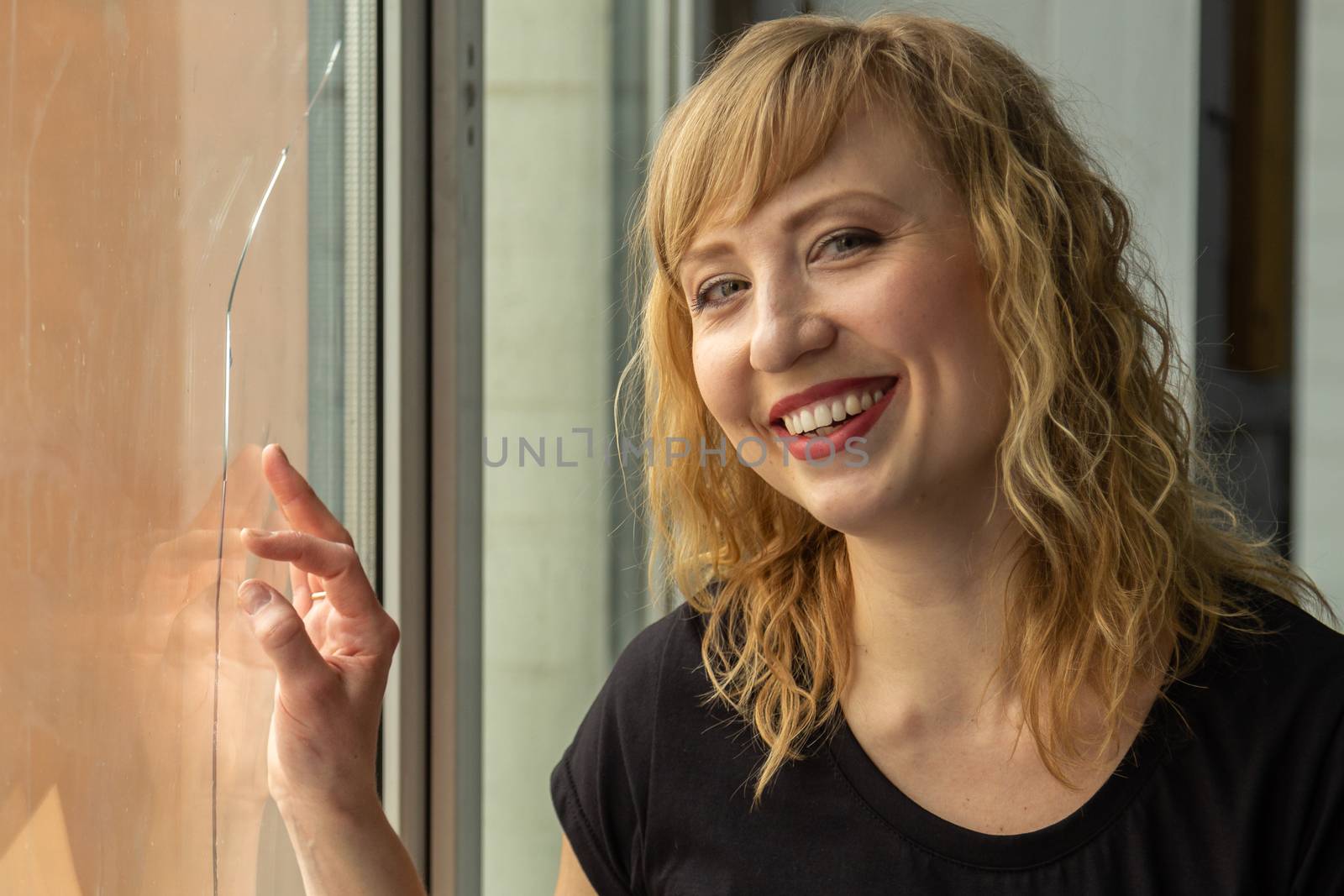 A woman of 30 years with blond hair near the window, you can see her reflection. Close-up