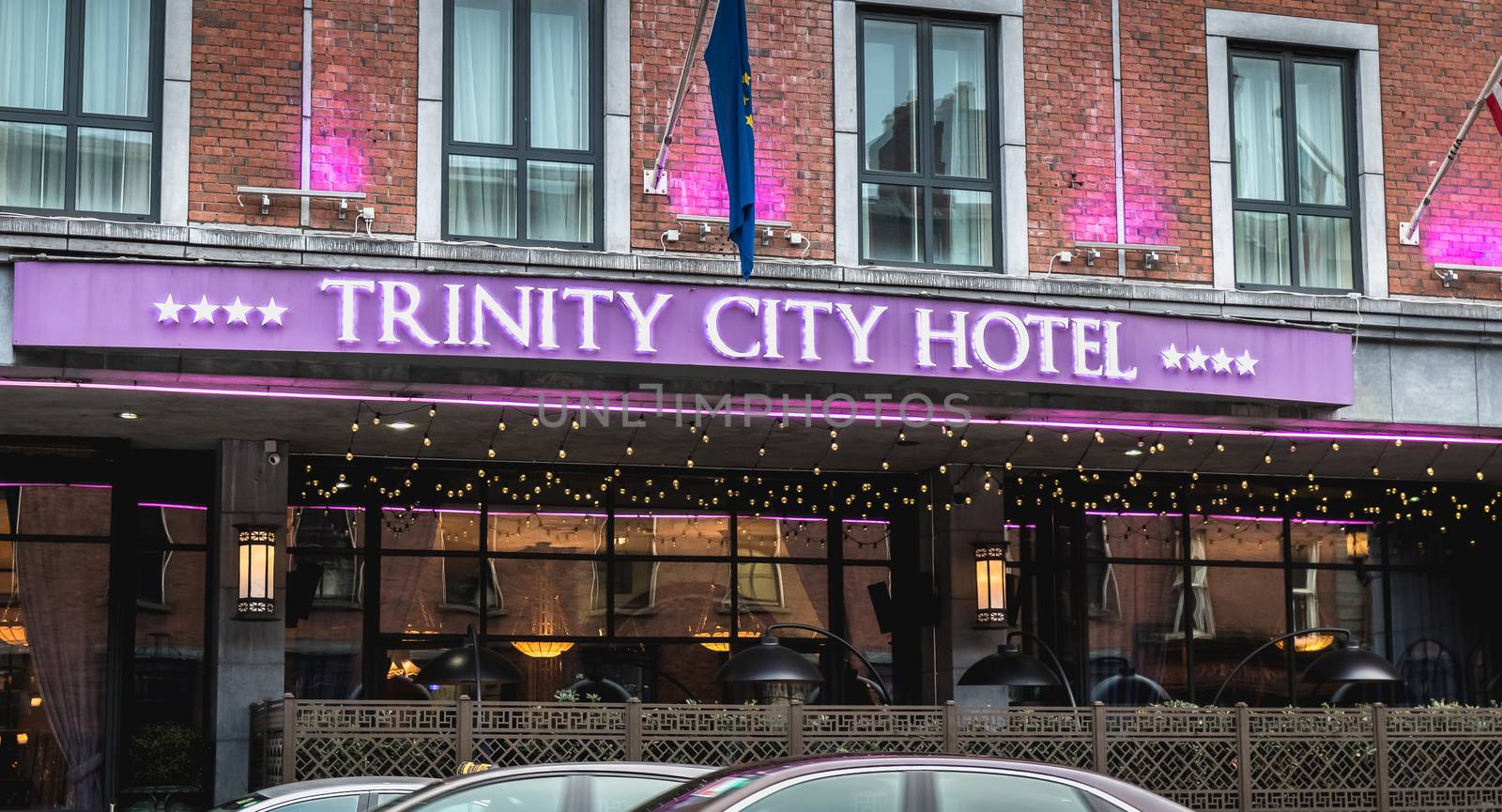 Dublin, Ireland - February 11, 2019: People and cars driving past the facade of the luxurious Trinity City Hotel in the city center on a winter day