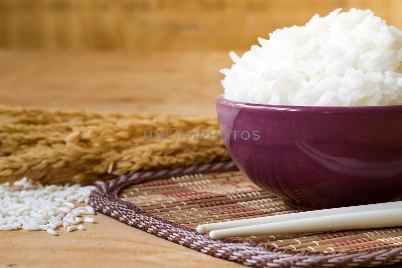 Cooked rice in bowl with raw rice grain and dry rice plant on  wooden table background.