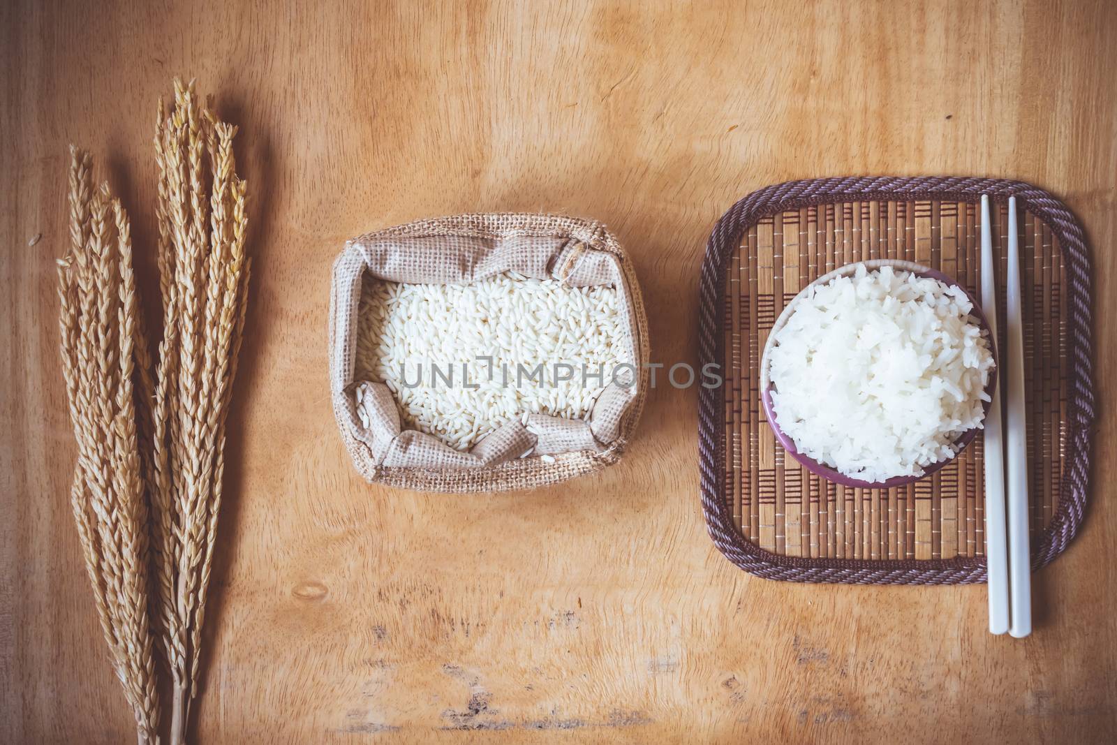 Cooked rice in bowl with raw rice grain and dry rice plant on  wooden table background.