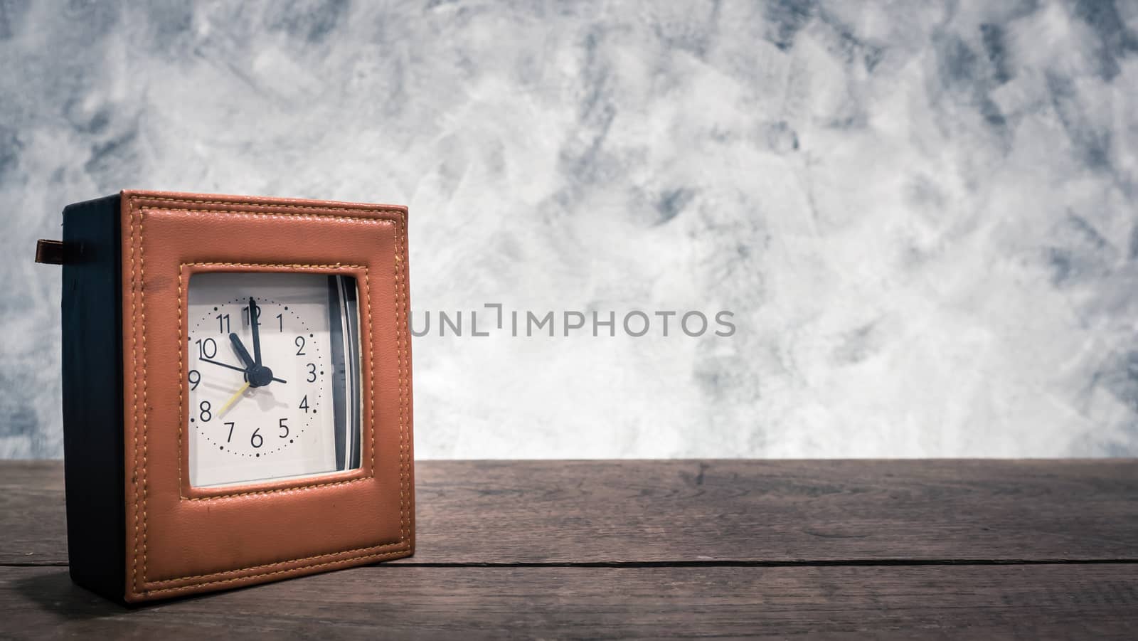Clock on the wooden table with vintage wall background.Free space for your text.