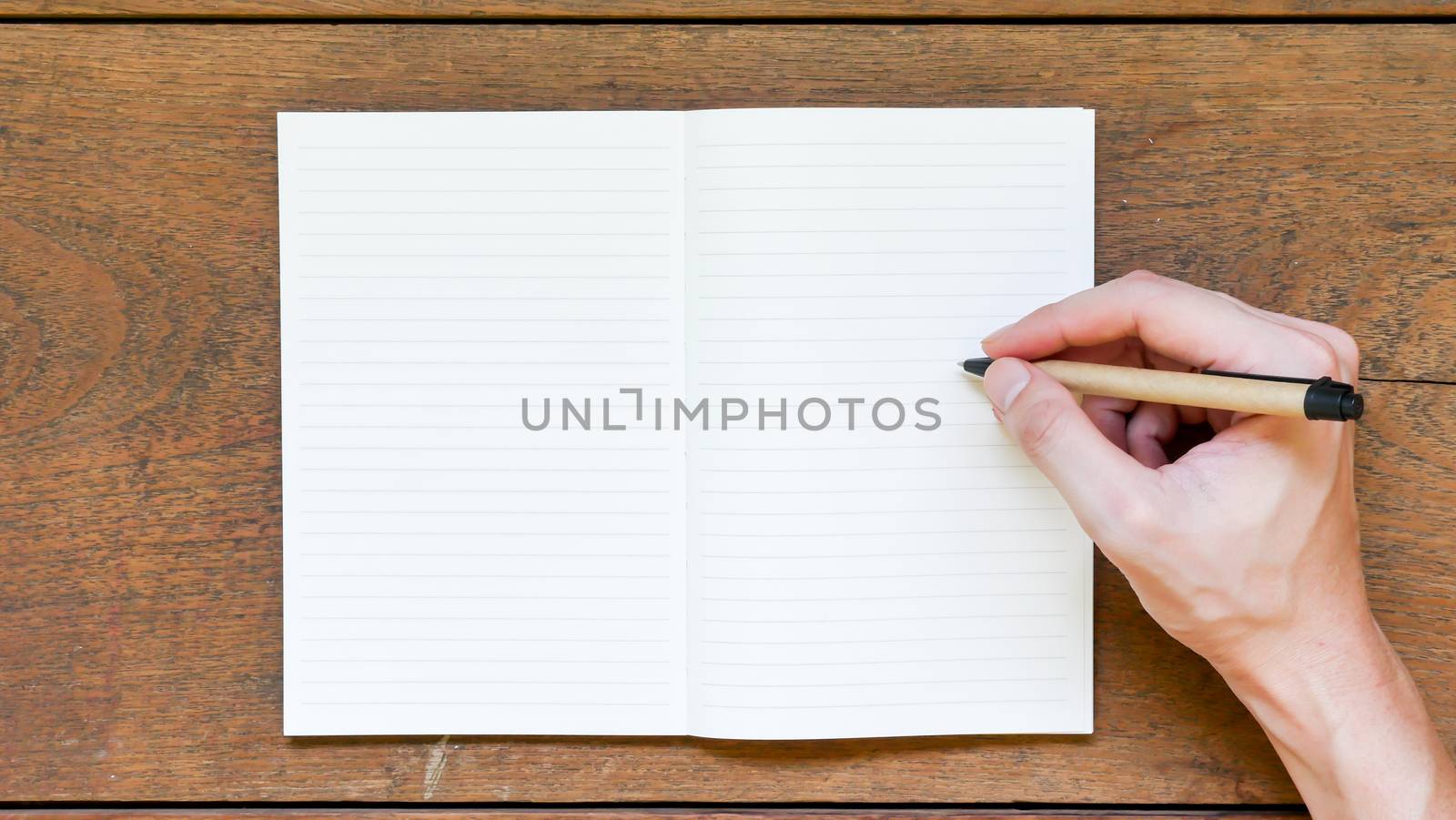 Man hands with pen writing on empty notepad over wooden table.