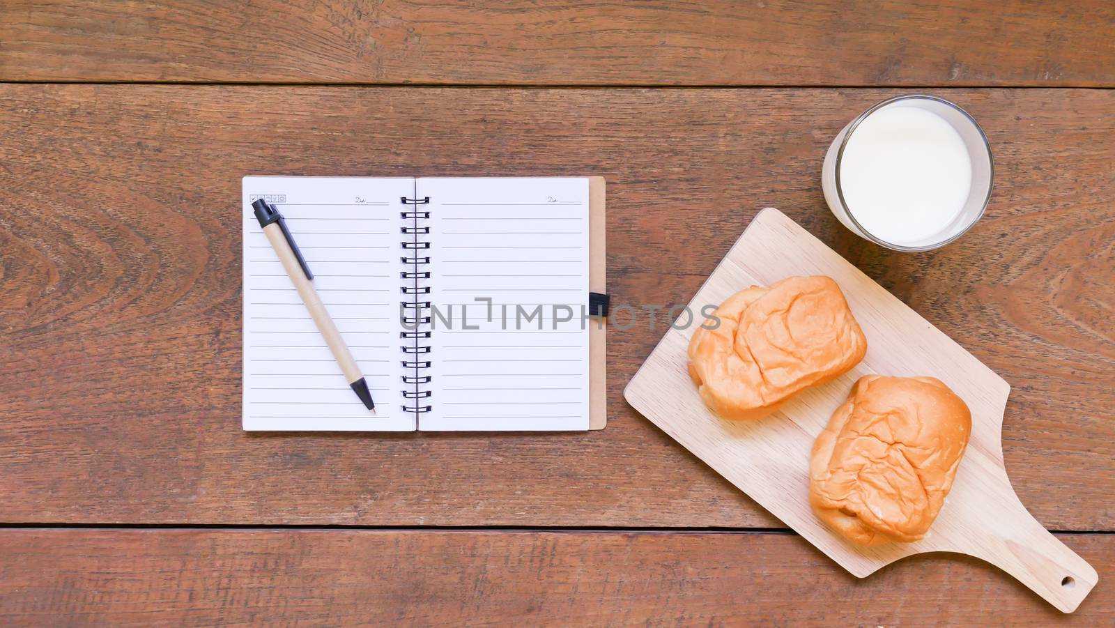 Notebook with bread and cup of milk on wooden table background.