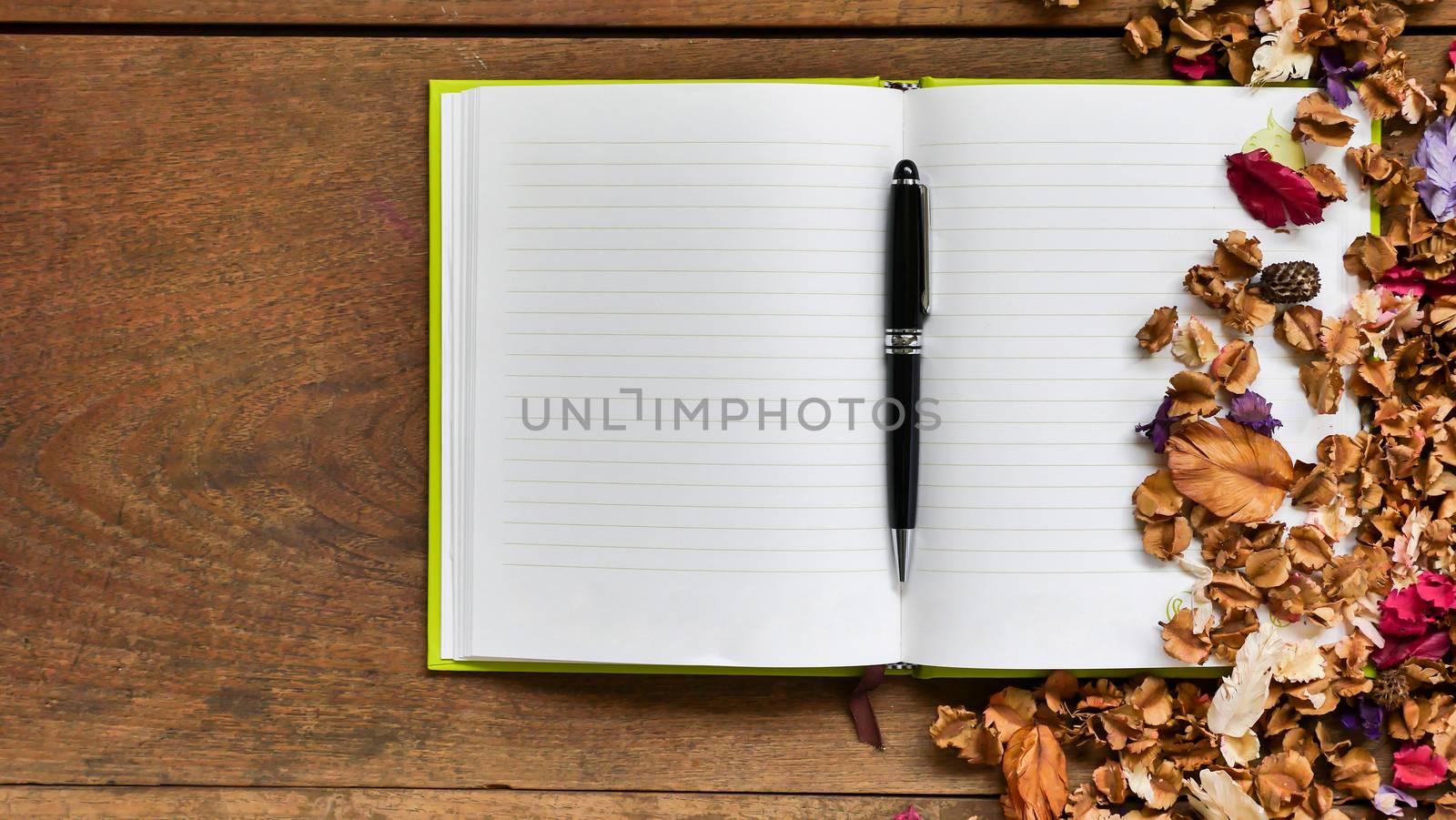 Top view workspace with blank notebook,pen and dried flowers on wooden table background .