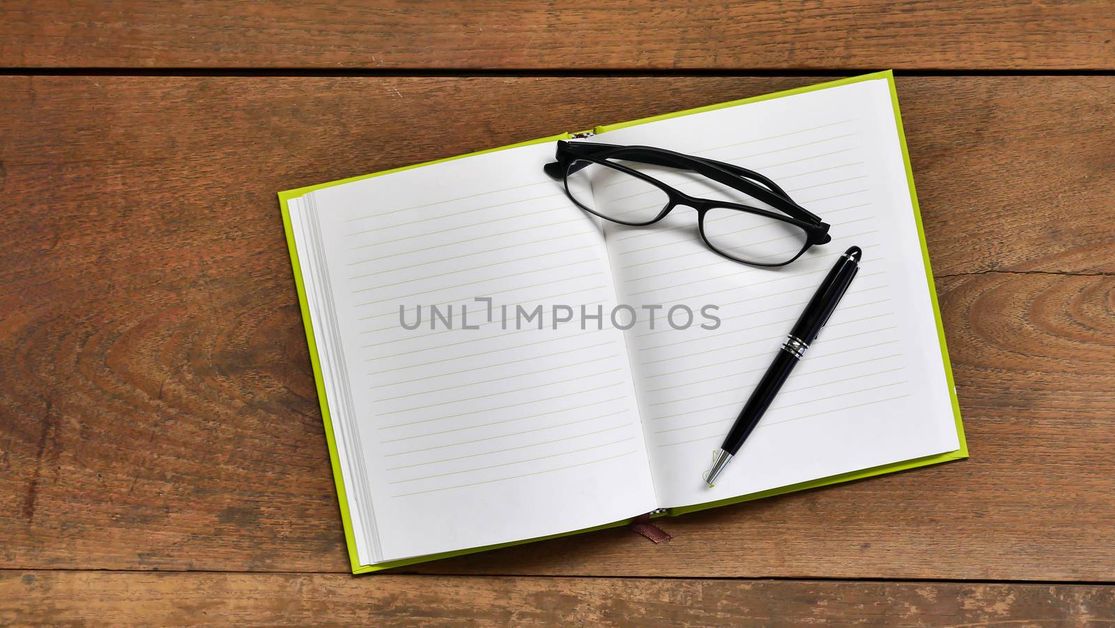 Top view workspace with blank notebook ,glasses and pen on wooden table background .