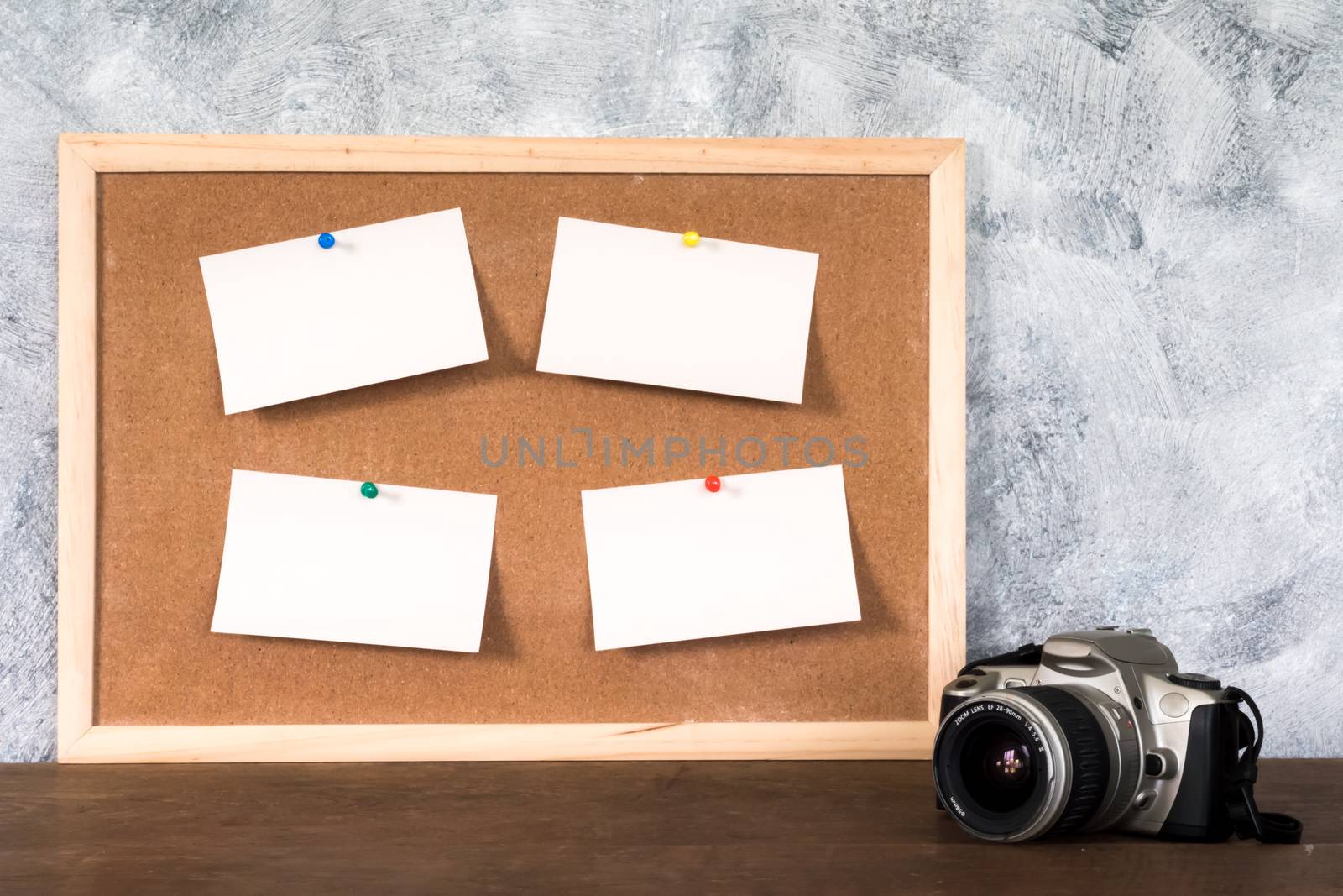 Blank papers pin up on cork board and camera over wooden table with textured background.