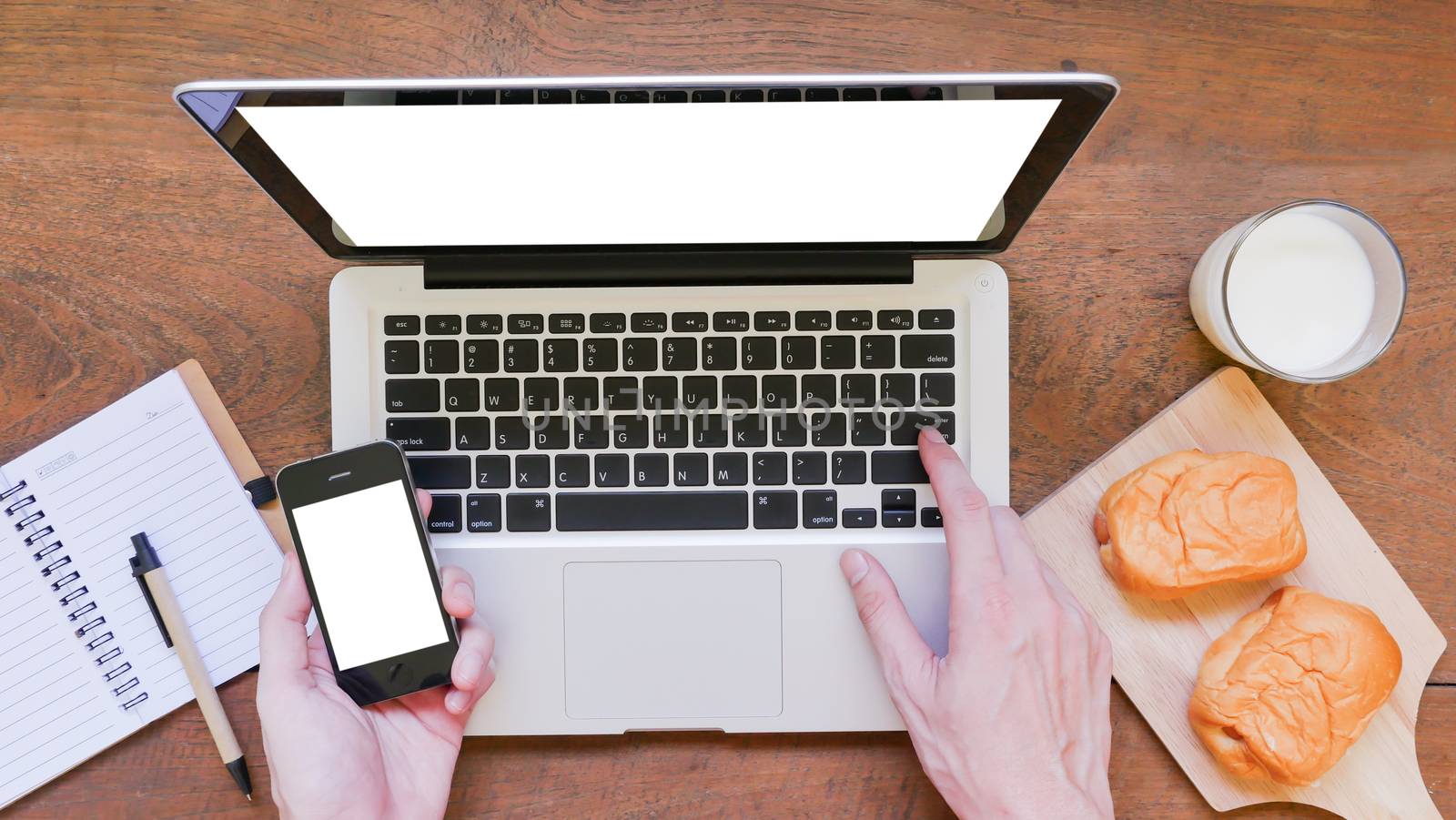 Labtop,notebook,
mobile phone and breakfast with hands on wooden table background.