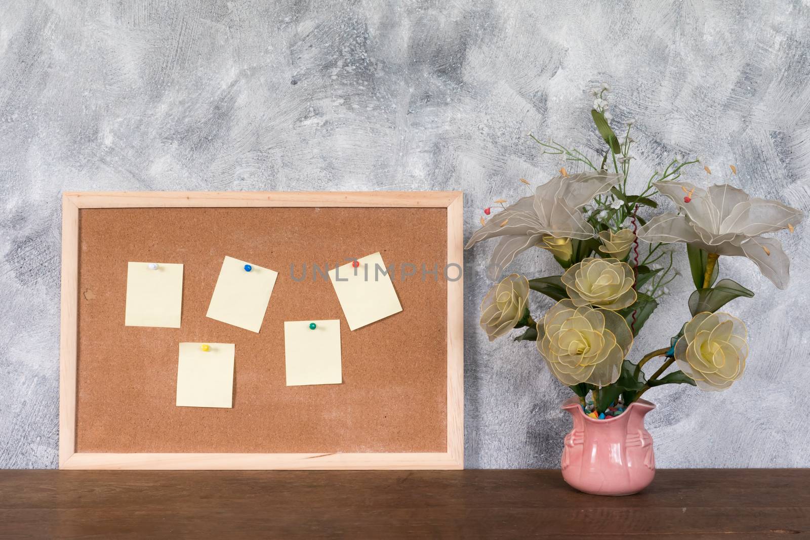 Blank papers pin up on cork board and flower vase over wooden table with textured background.