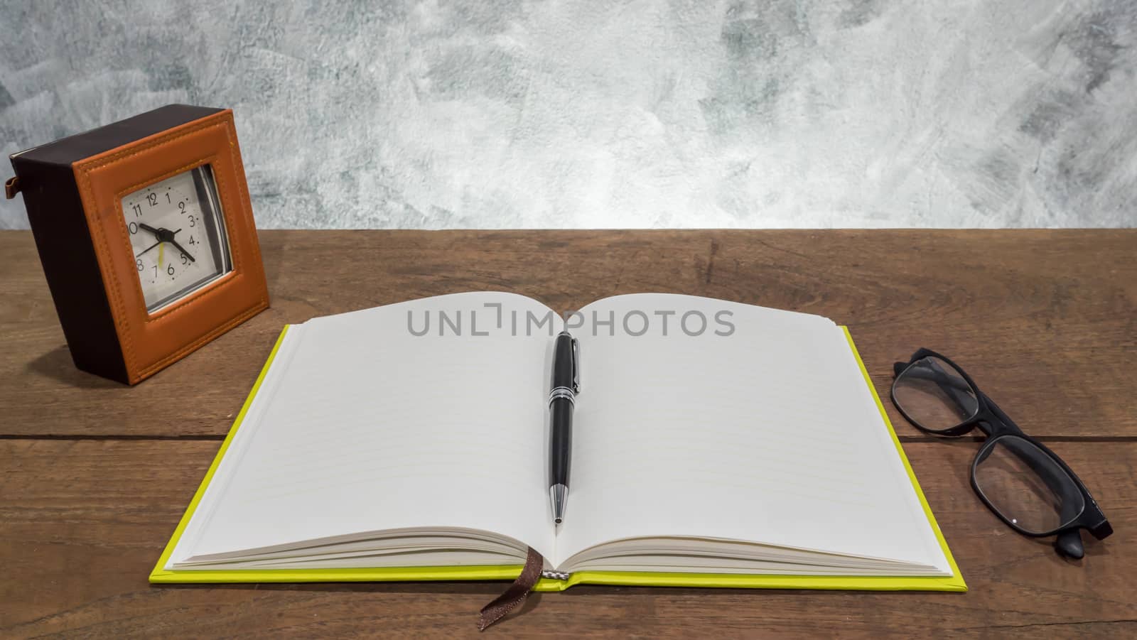 Blank notebook with pen,clock  and glasses on wooden table.