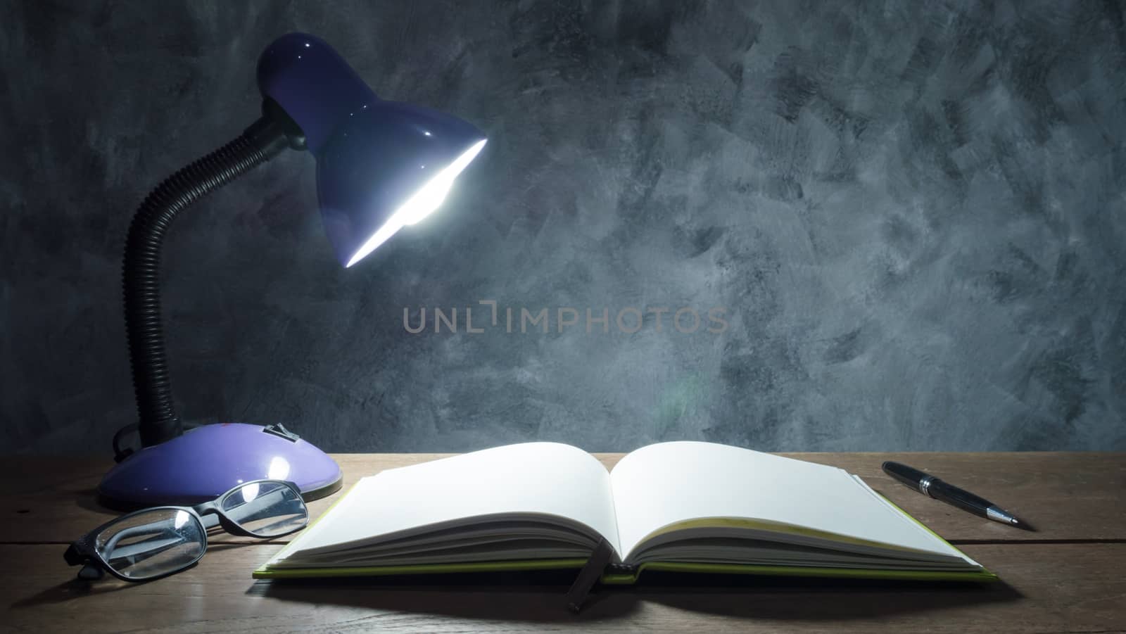 Lamp with notebook,pen and glasses  on  wooden table with vintage wall background.